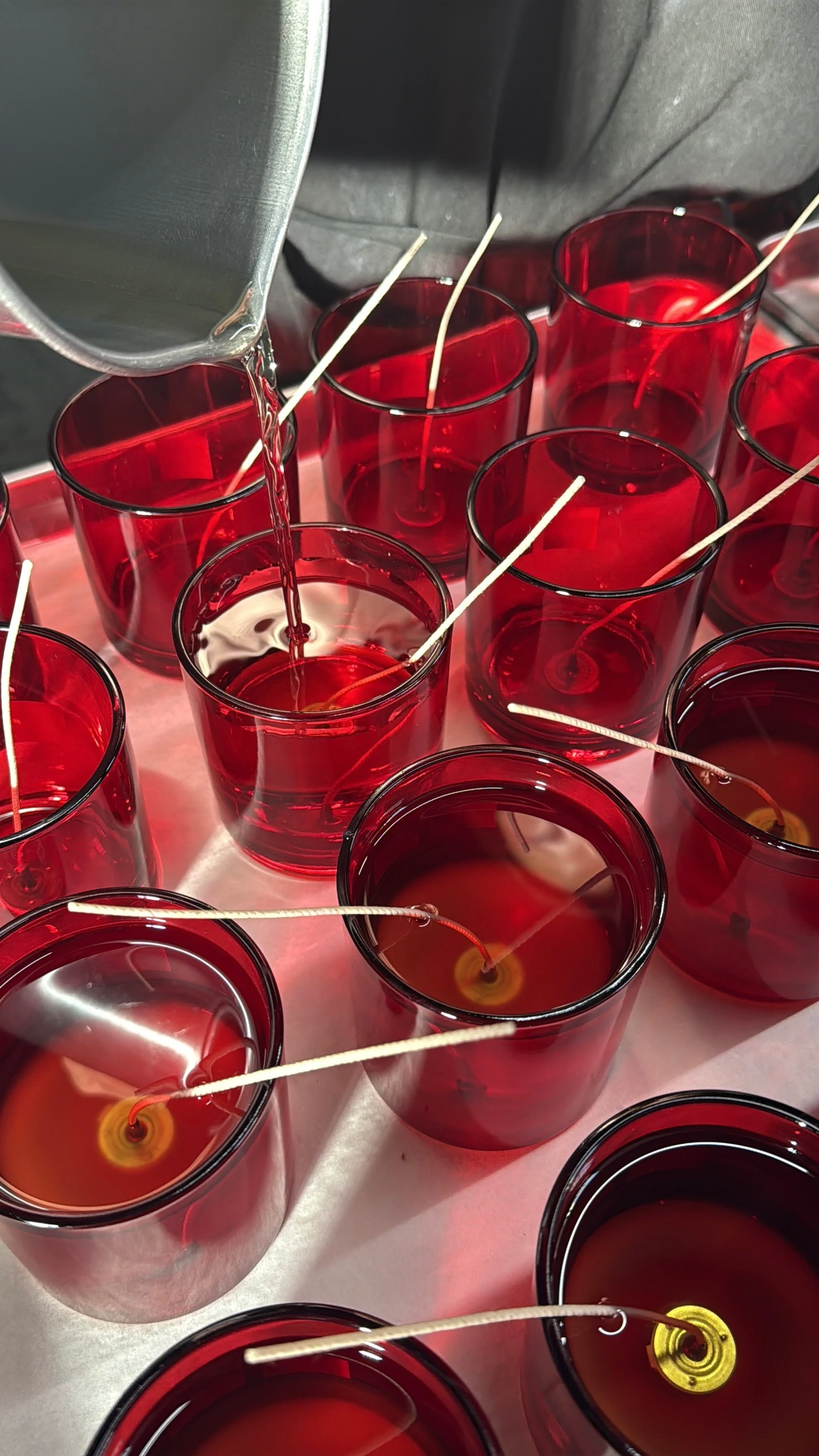 Behind the scenes candle pouring into red glass vessels during the production process