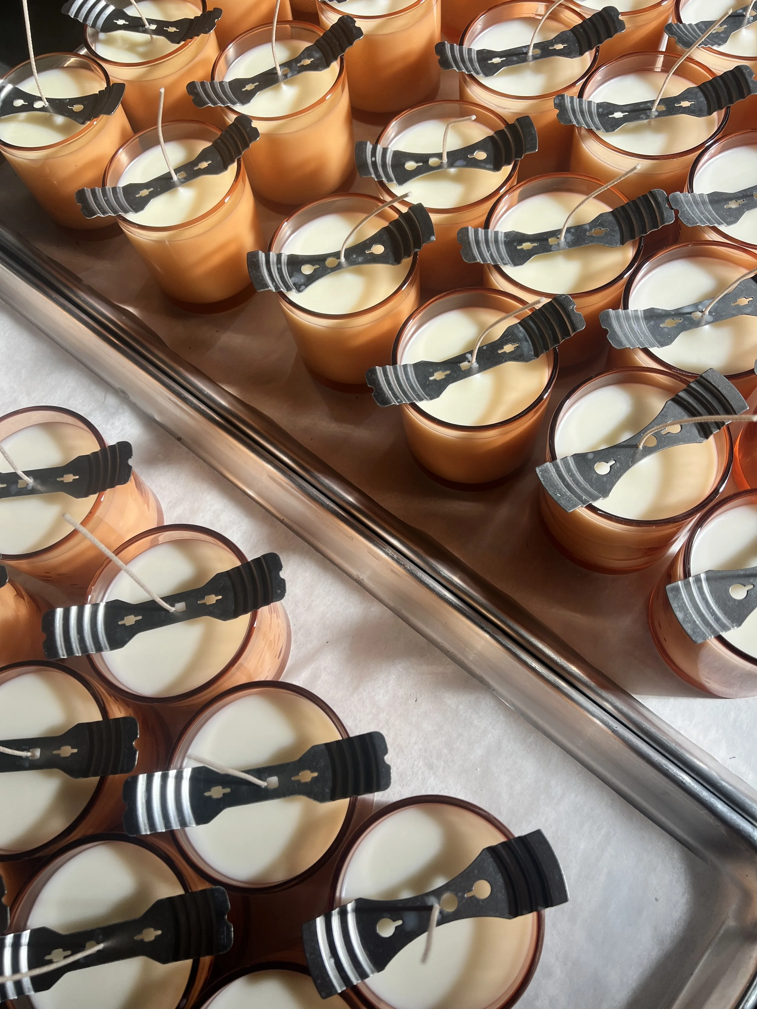 Candle wicks being centered using tools during production in orange amber glass vessels