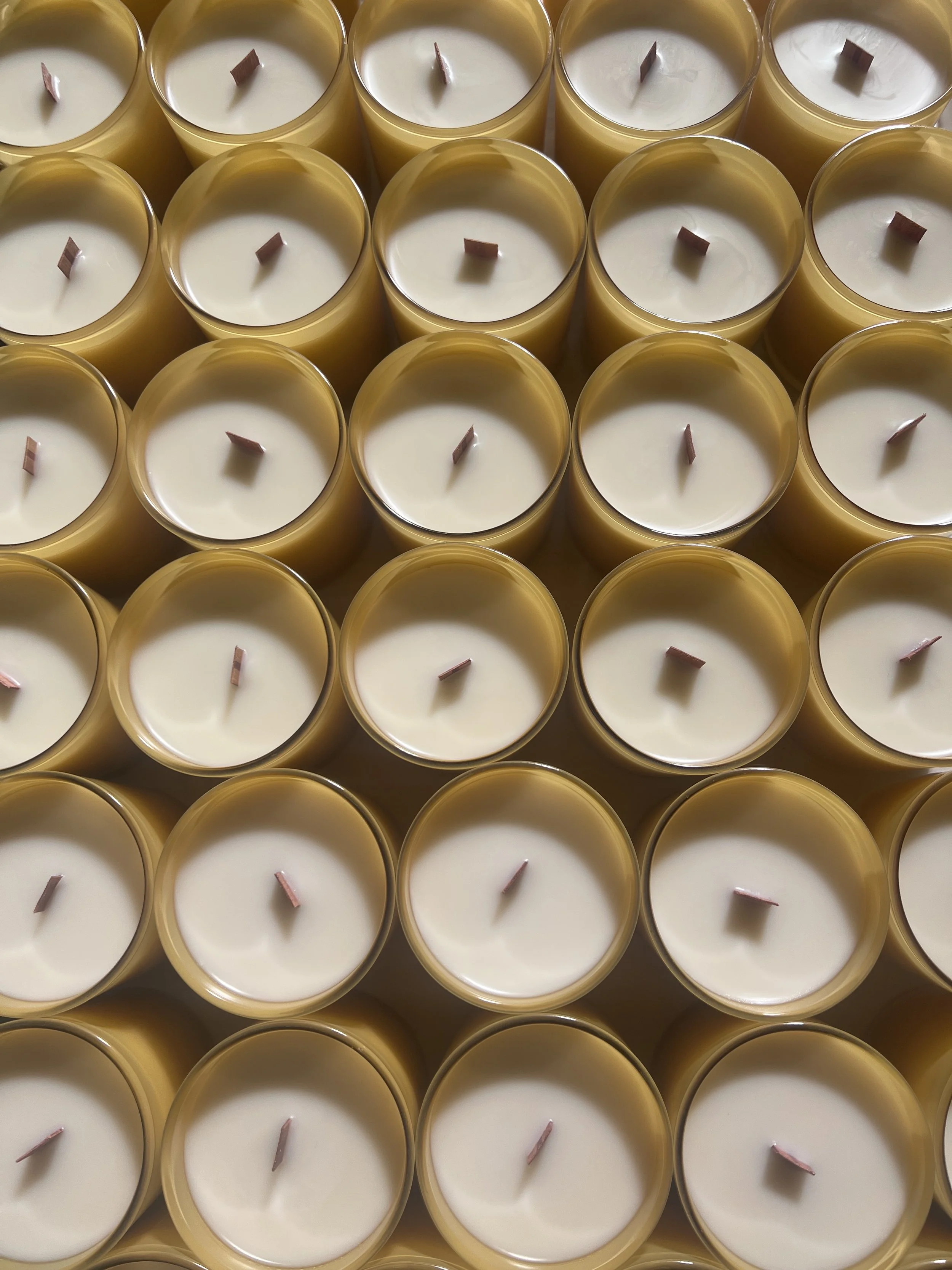 Hand poured candles curing in yellow glass vessels during the candle manufacturing process