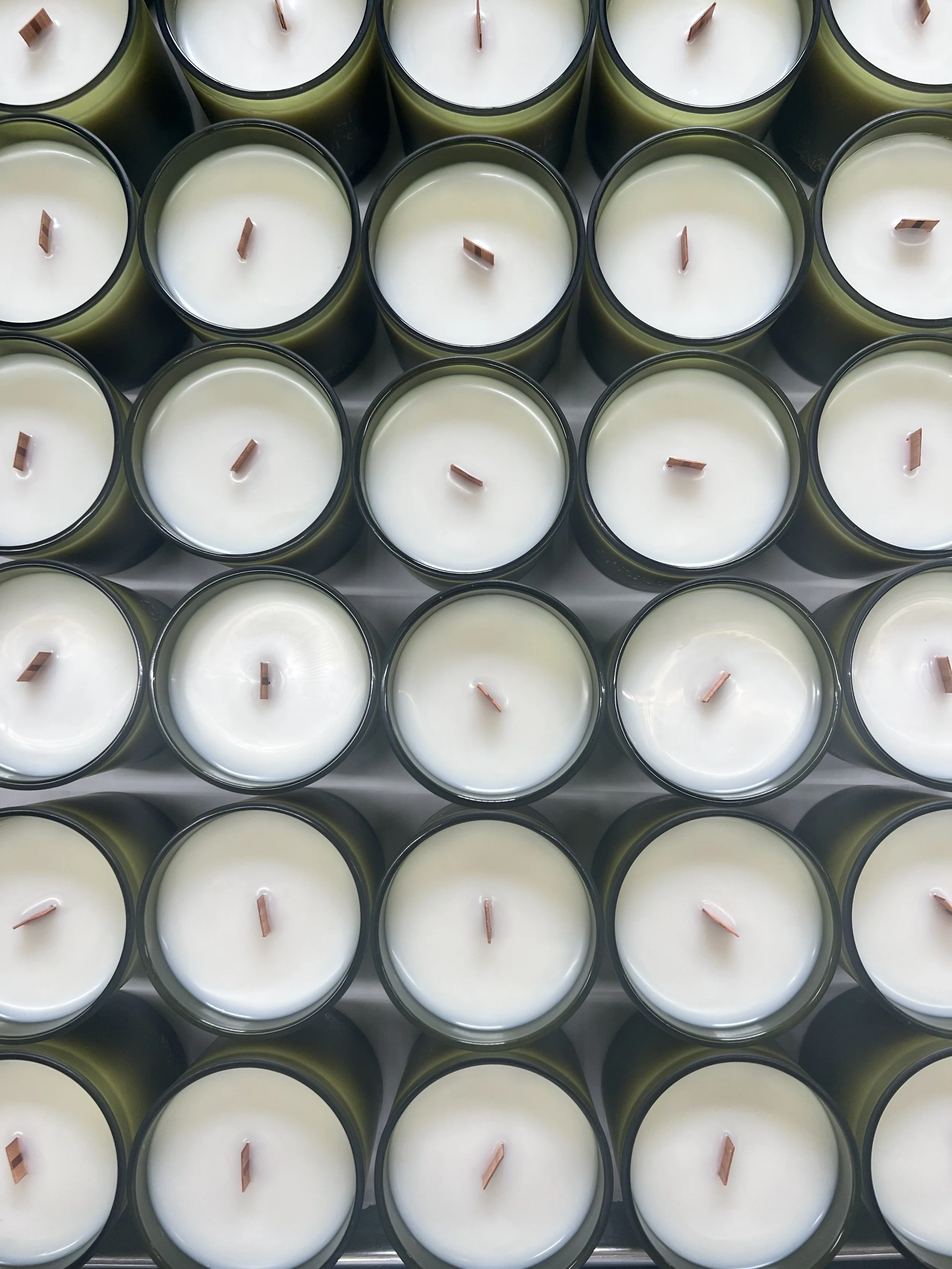 Behind the scenes candle production with hand poured candles in green glass vessels during private label manufacturing