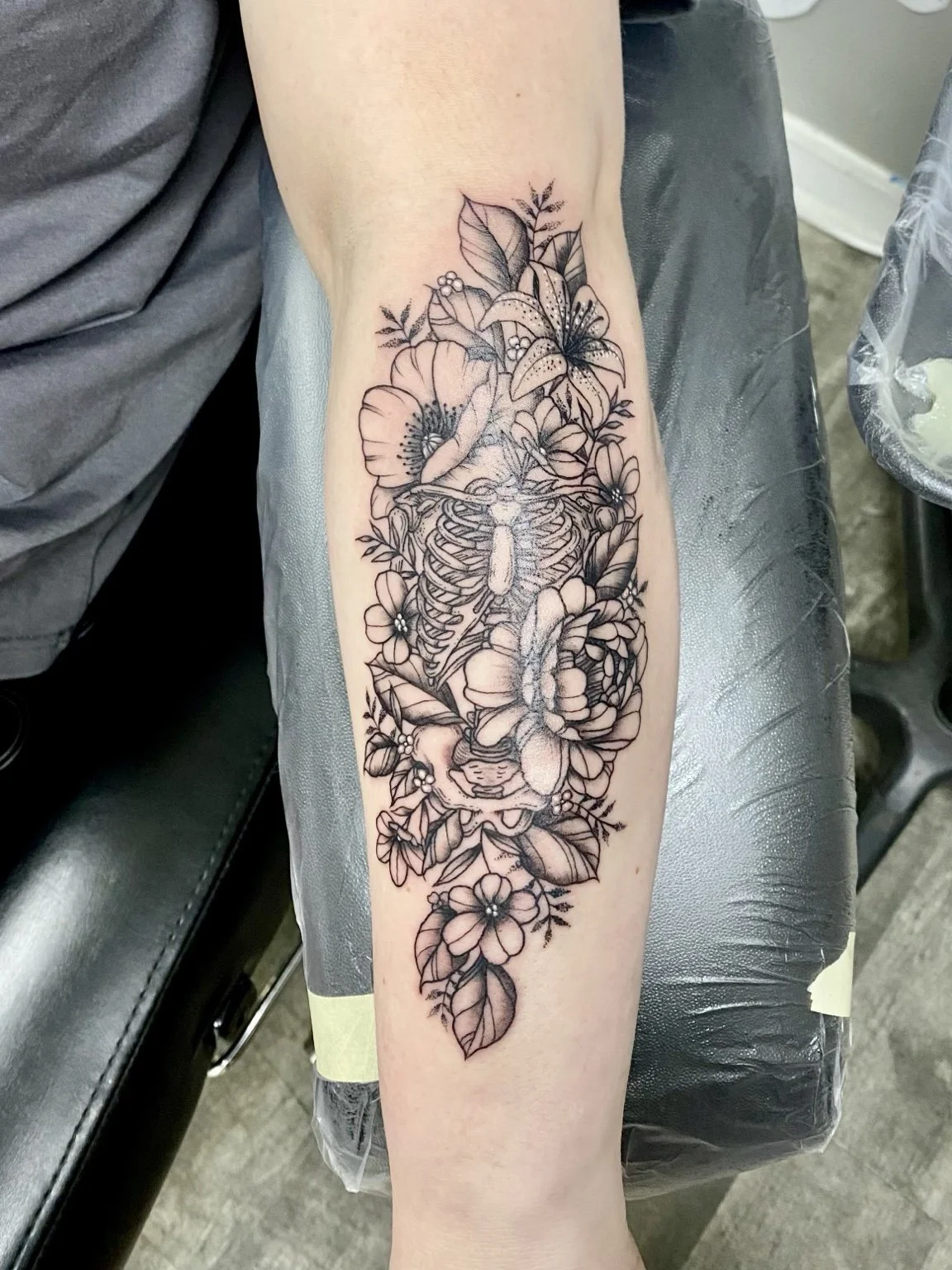 Black-and-grey skeleton and flowers forearm tattoo by Liz House