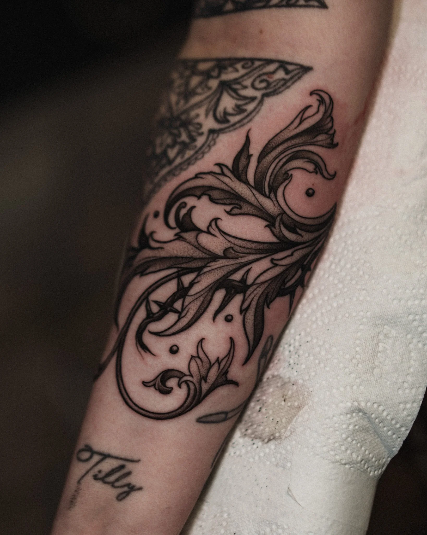 Close-up of a tattoo on a person's arm, featuring ornate black floral and swirl designs. Dark fantasy inspired tattoo by Jason James Smith