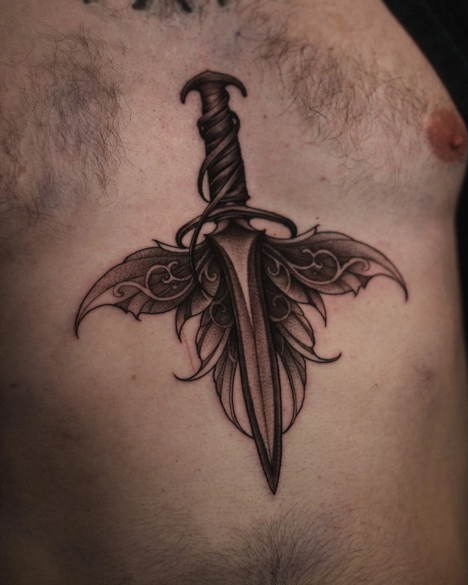 Close-up of a tattoo of a sword with wings on a person's chest.
