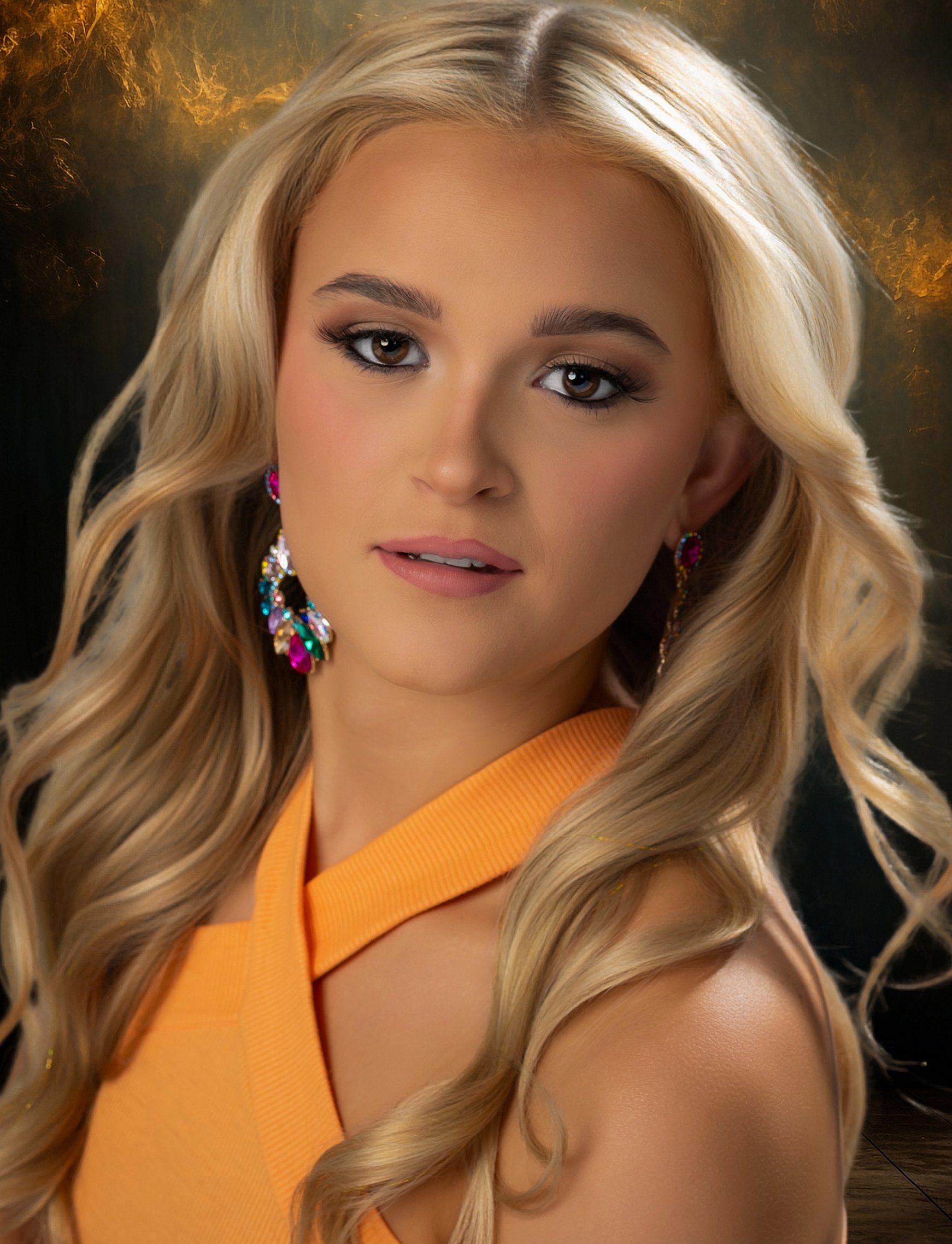 A woman with long, blonde, wavy hair wearing colorful earrings and a yellow top, looking slightly to the right, with a blurred background.