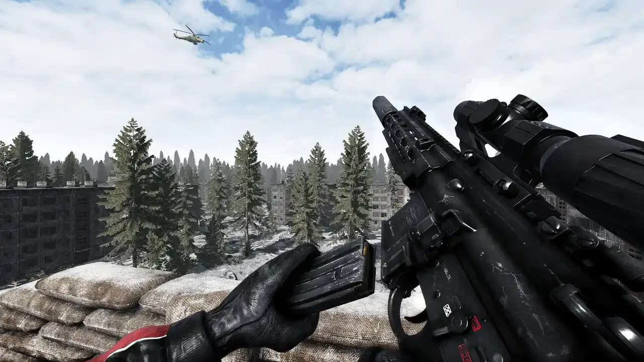 A first-person gameplay screenshot from Road to Vostok showing a player reloading an assault rifle in a snowy, abandoned urban environment with a helicopter flying overhead.