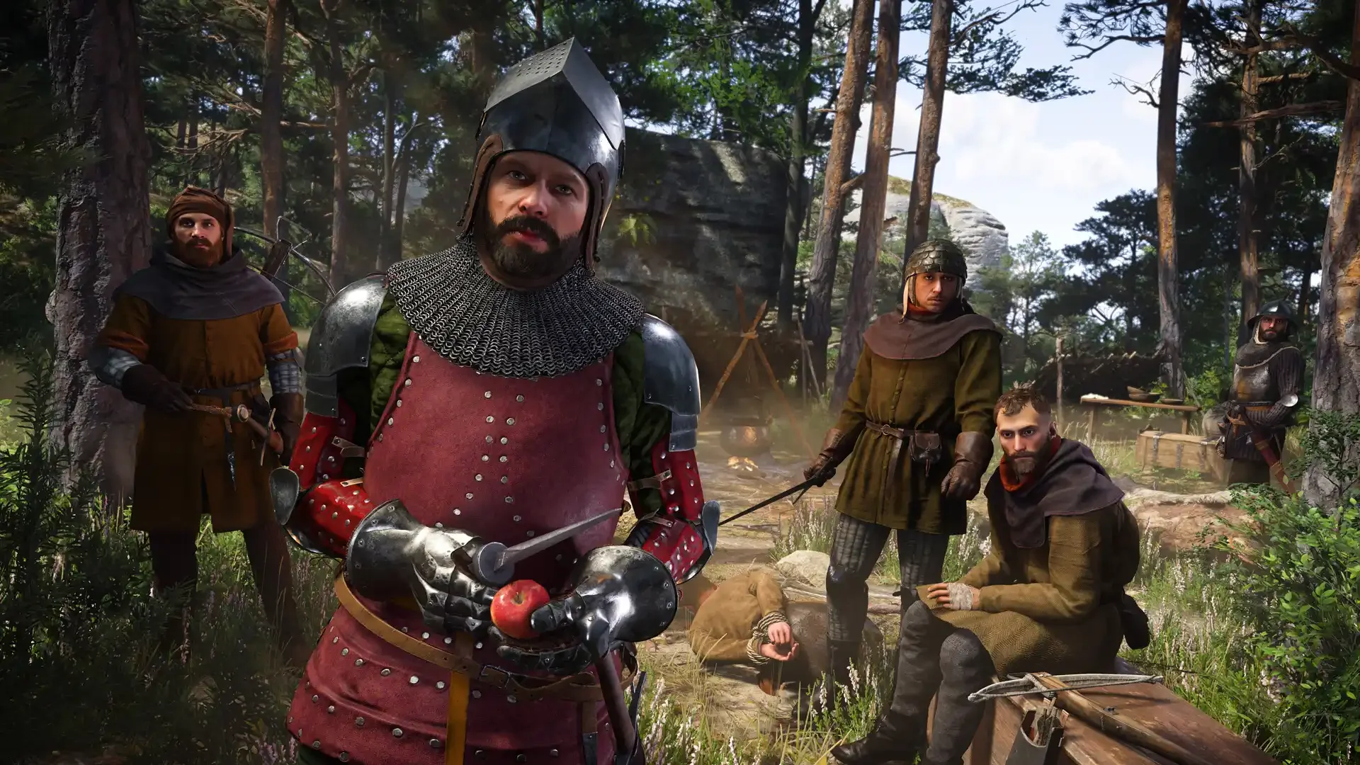 A screenshot from Kingdom Come: Deliverance II showing a heavily armored man in a red gambeson holding an apple and a dagger, surrounded by his rough-looking companions in a detailed forest encampment.
