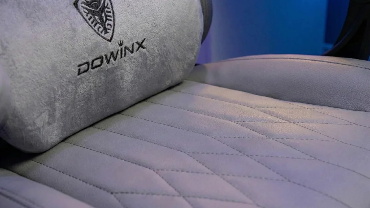 Close-up of a white leather Dowinx gaming chair seat with diamond stitching and an embroidered grey velour lumbar pillow.