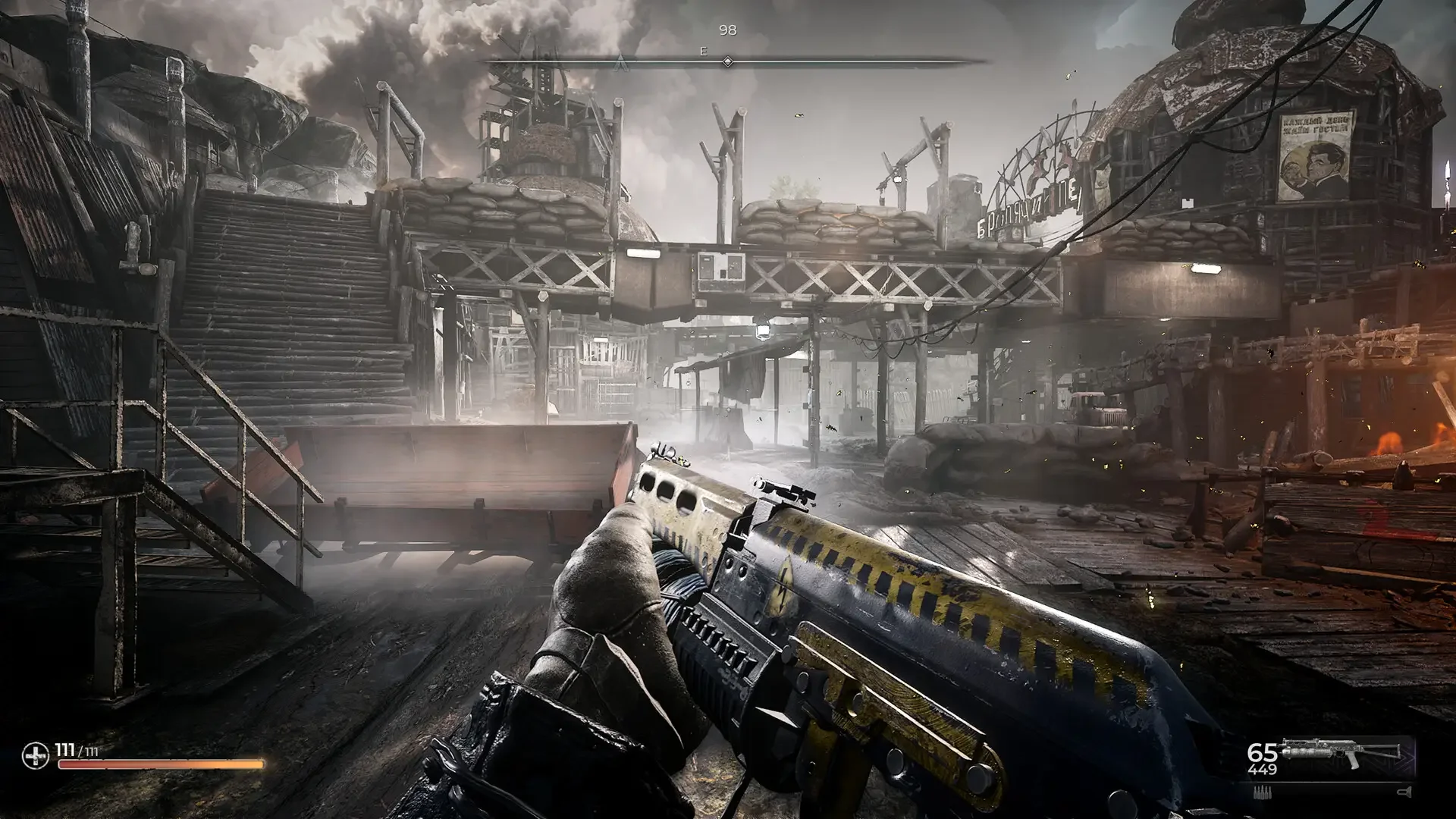 A first-person gameplay screenshot from PIONER showing the player's custom rifle aimed toward a muddy, heavily fortified Eastern Bloc shantytown built of wood and sandbags.