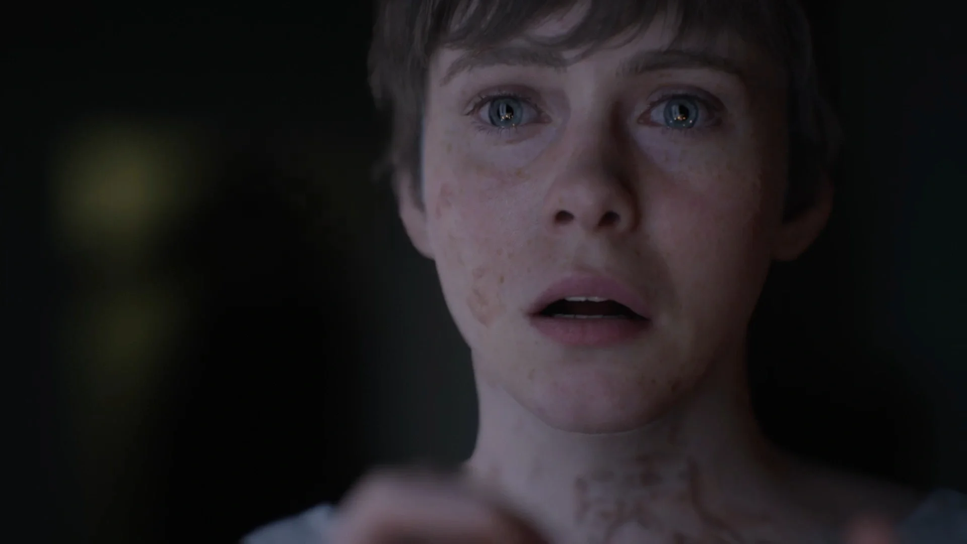 A close-up screenshot from the game OD showing a young woman (Sopha Lillis) with pale skin, blue eyes, and reddish marks or freckles on her face and neck, looking terrified in the dark.