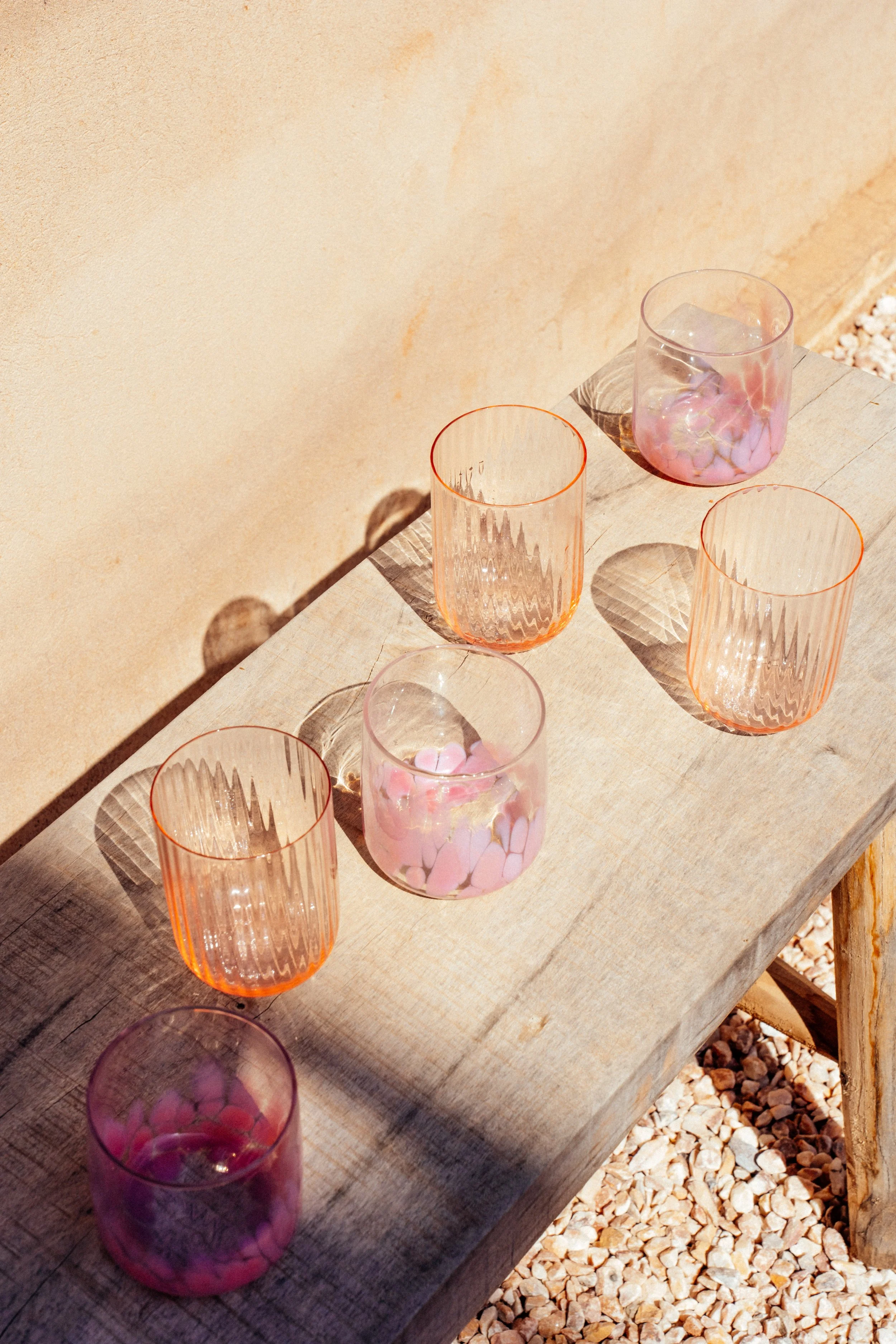 Sechs bunte Gläser mit unterschiedlichen Mustern und Farben auf einem Holztisch, Schatten auf die Wand, im Sonnenlicht