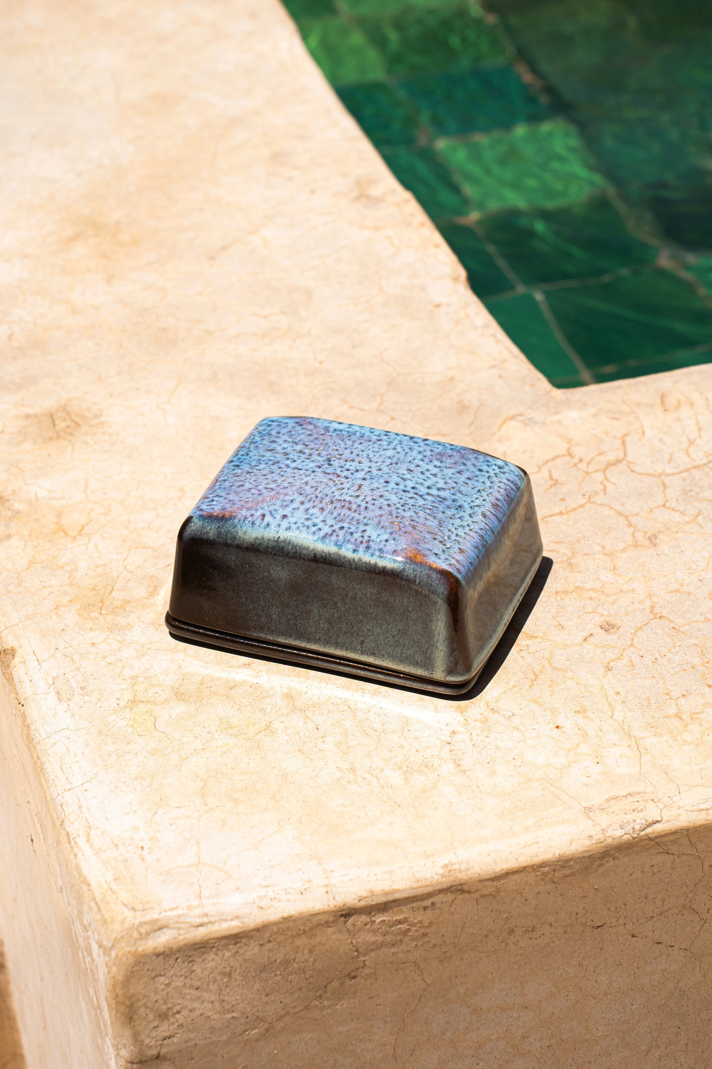 Keramiksoap in einer offenen Ablage neben einem Schwimmbad mit grünen Fliesen.