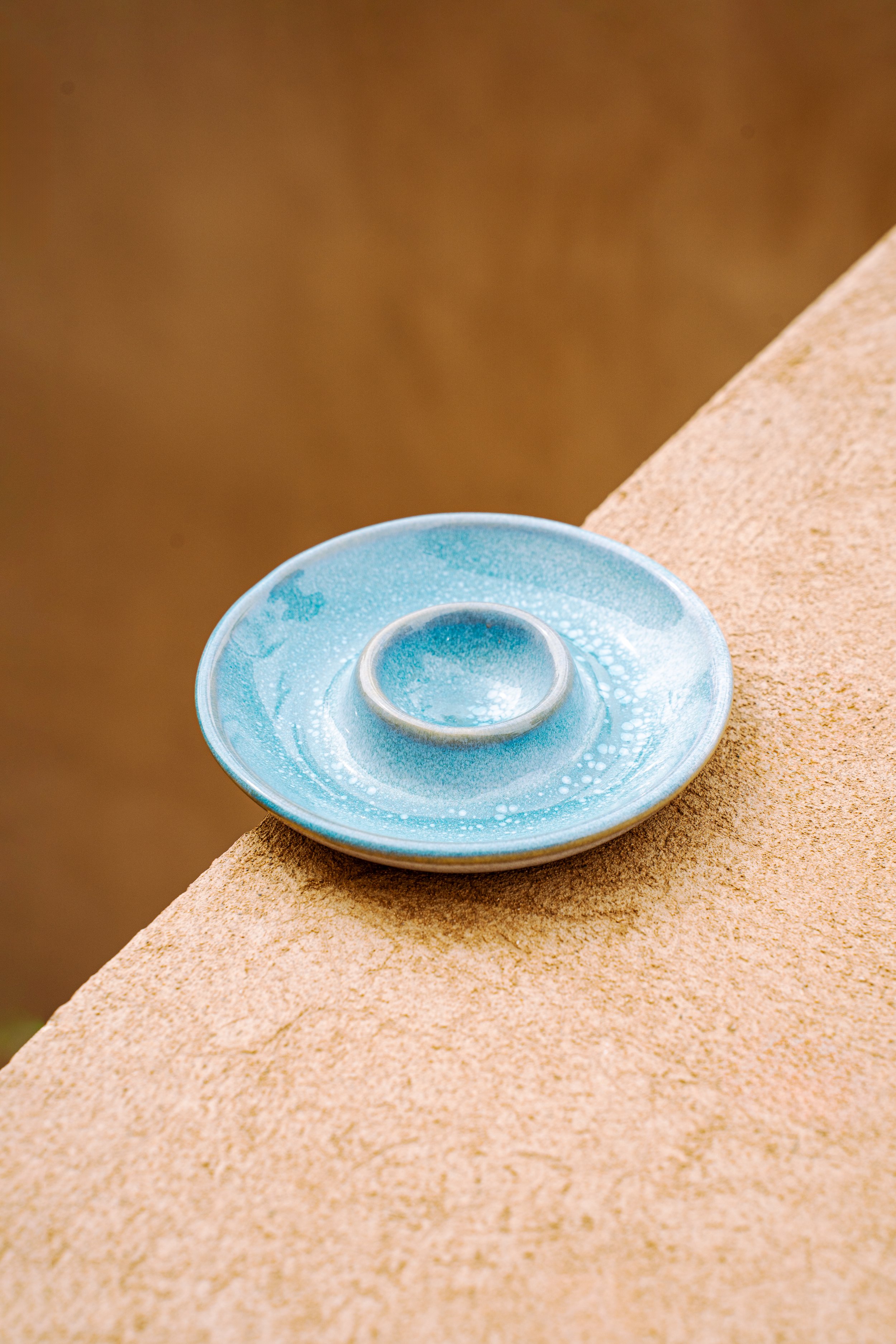 Blaue, keramikartige Kerzenhalter auf Sandstein, unscharfer brauner Hintergrund.