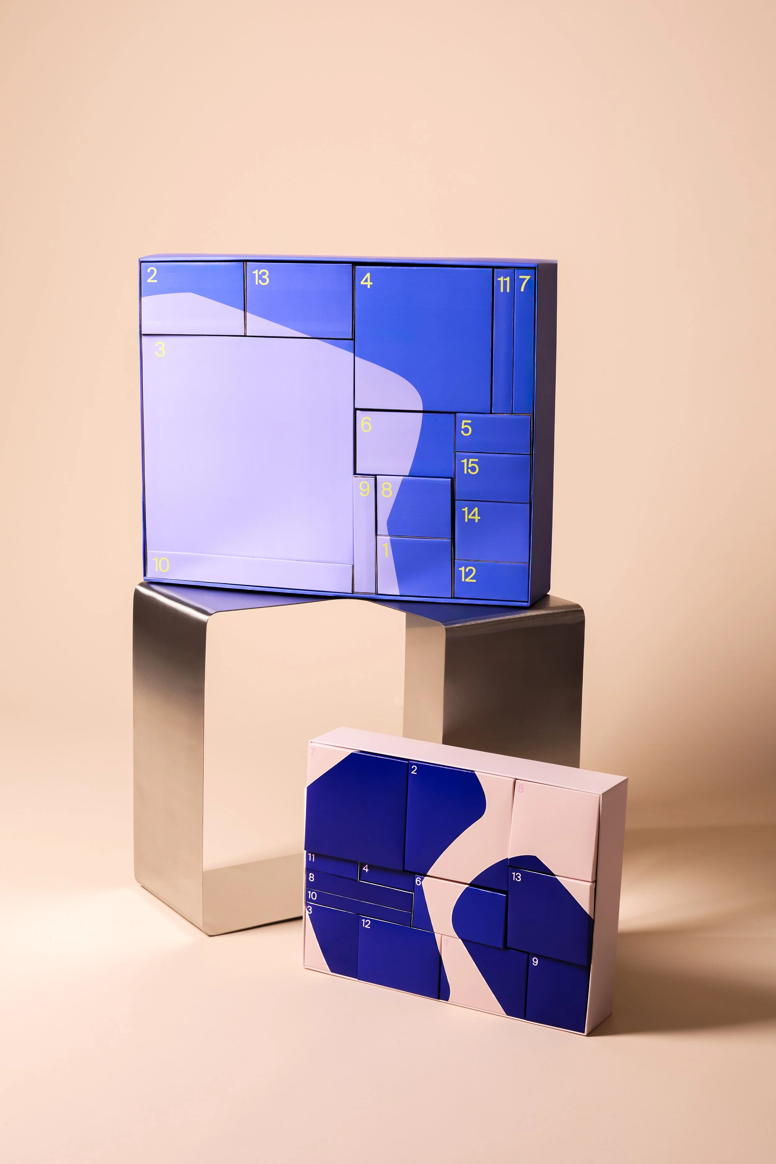 Zwei bunte Puzzles mit nummerierten Teilen, ein größeres blau-weißes Puzzle auf einem Metallständer und ein kleineres blau-weißes Puzzle auf dem Boden. Beide Puzzles haben abstrakte Designs.