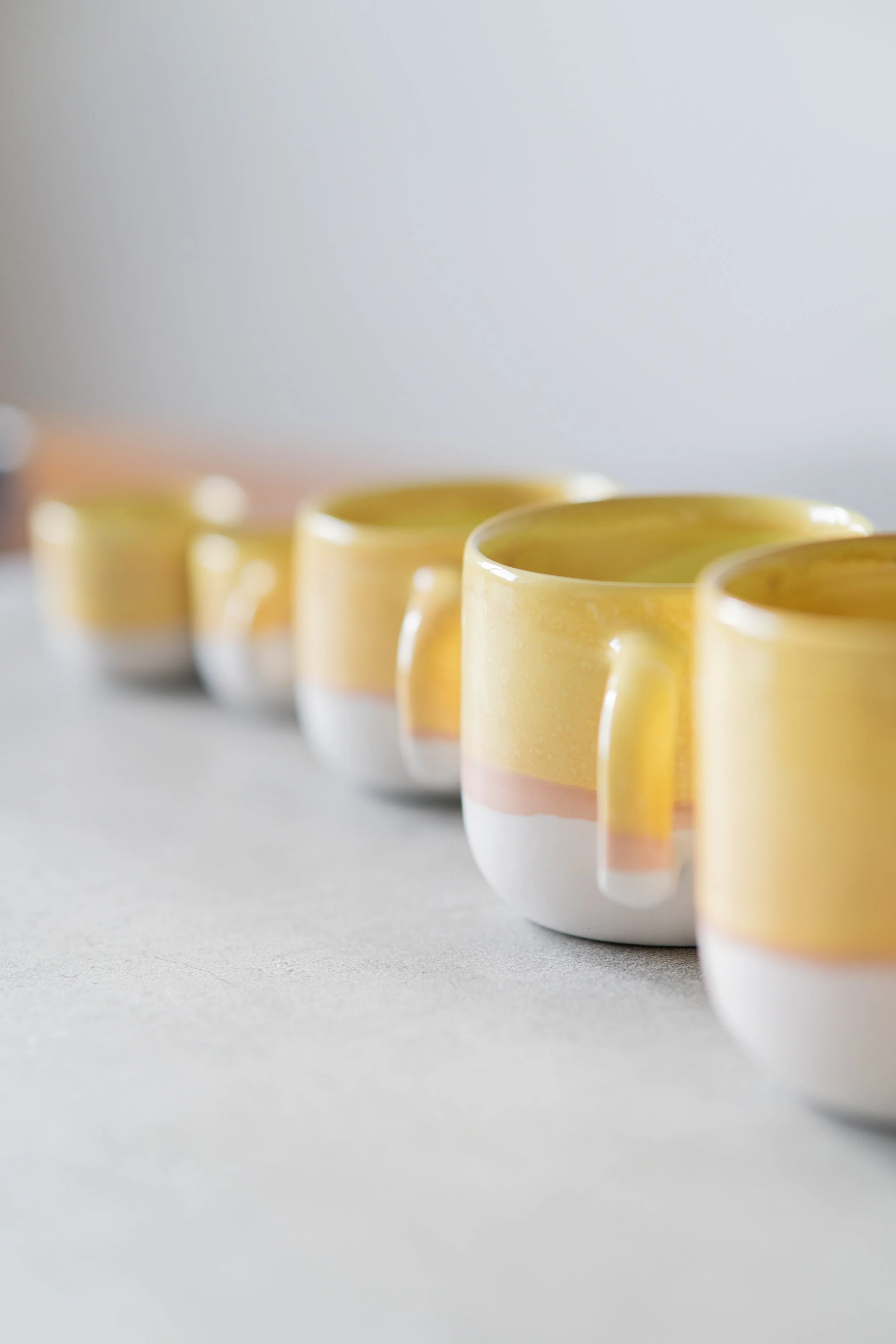 Fünf gelbe Tassen sind in einer Reihe auf einer weißen Oberfläche platziert.