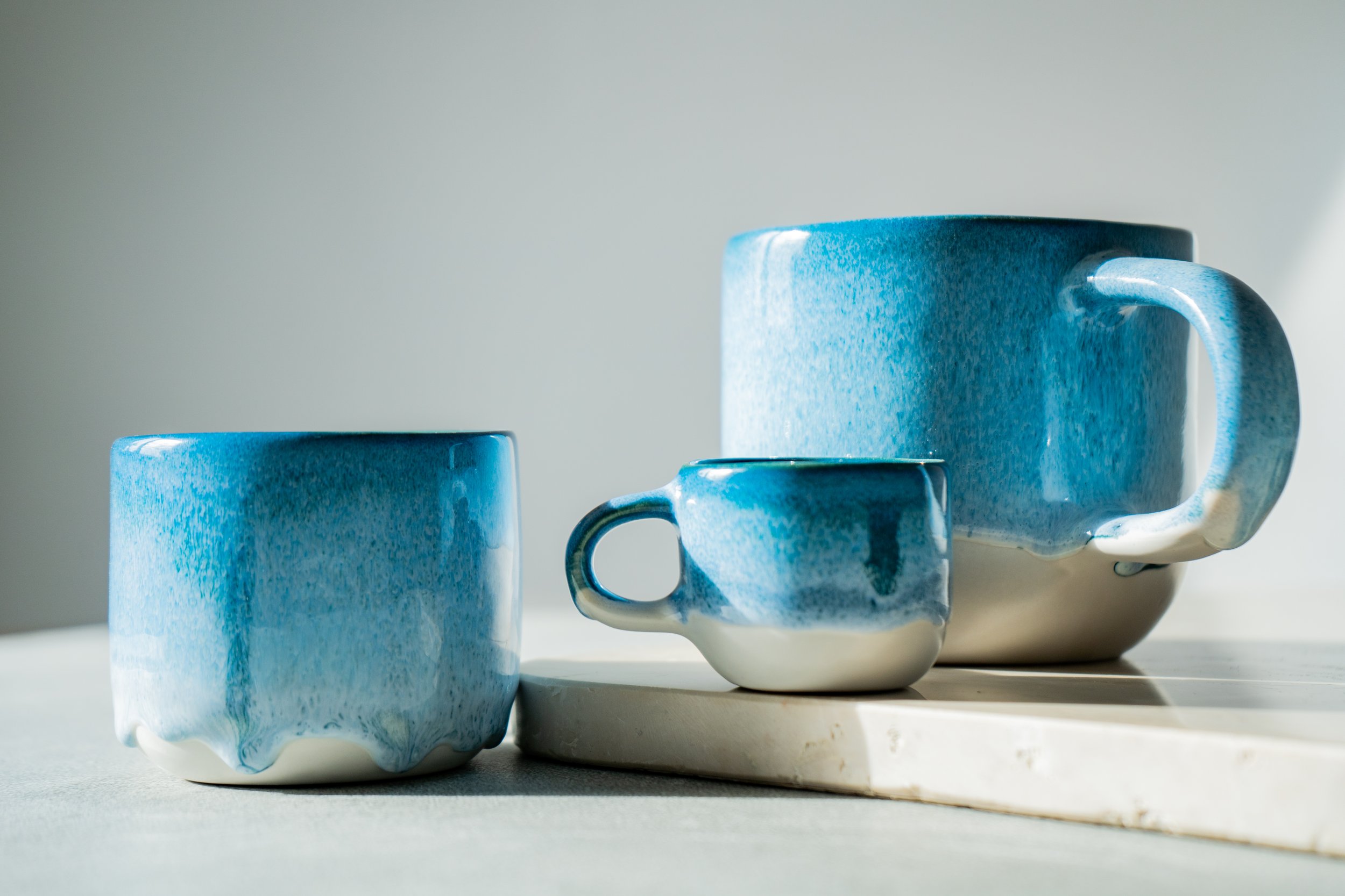 Drei blaugraue Keramikbecher unterschiedlicher Größe auf einer weißen Oberfläche
