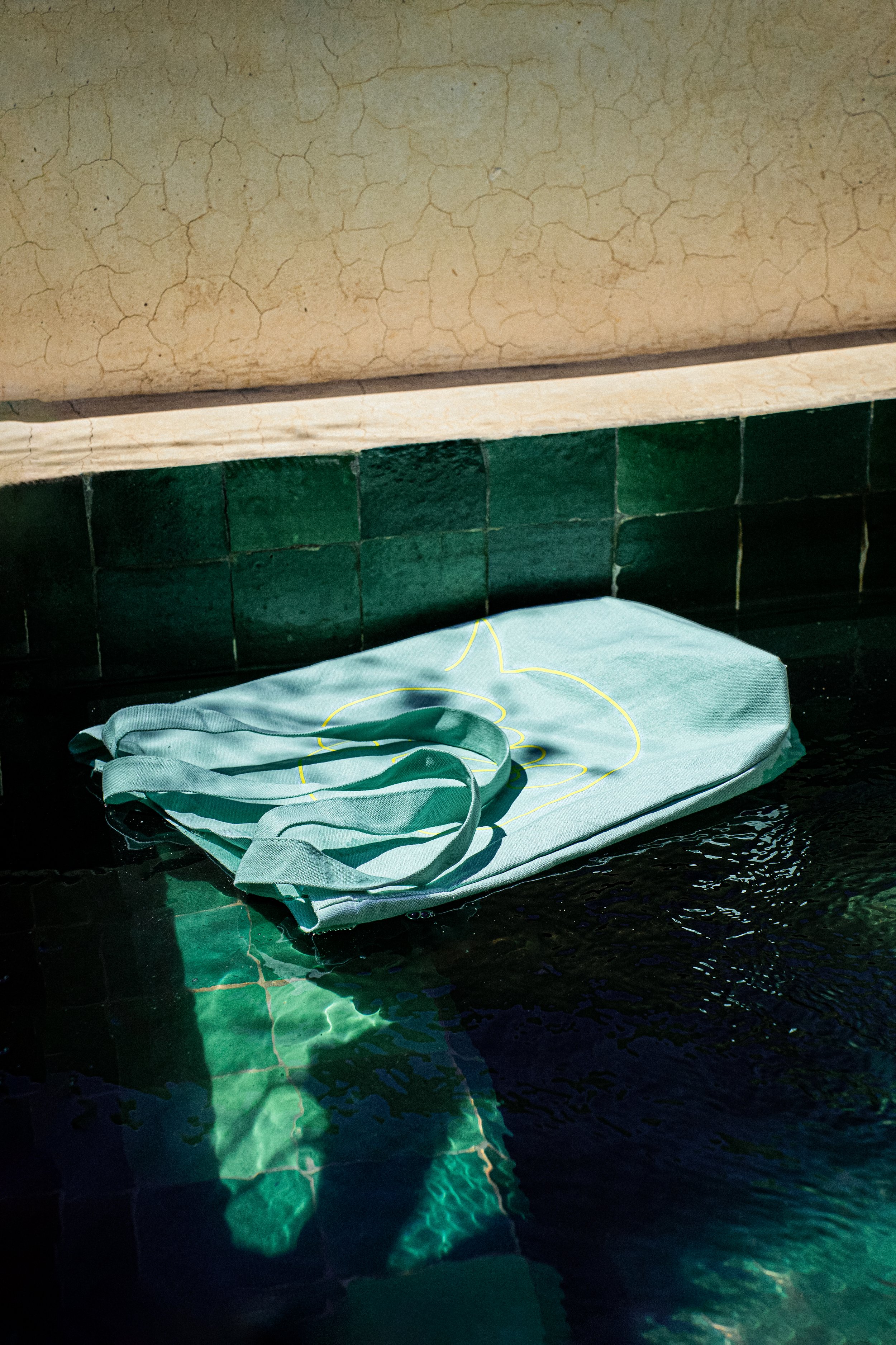 Ein eingepackter Stoffbeutel liegt auf einem schwarzen Fliesenboden neben einem Wasserbecken, der Beutel ist teilweise ins Wasser getaucht.