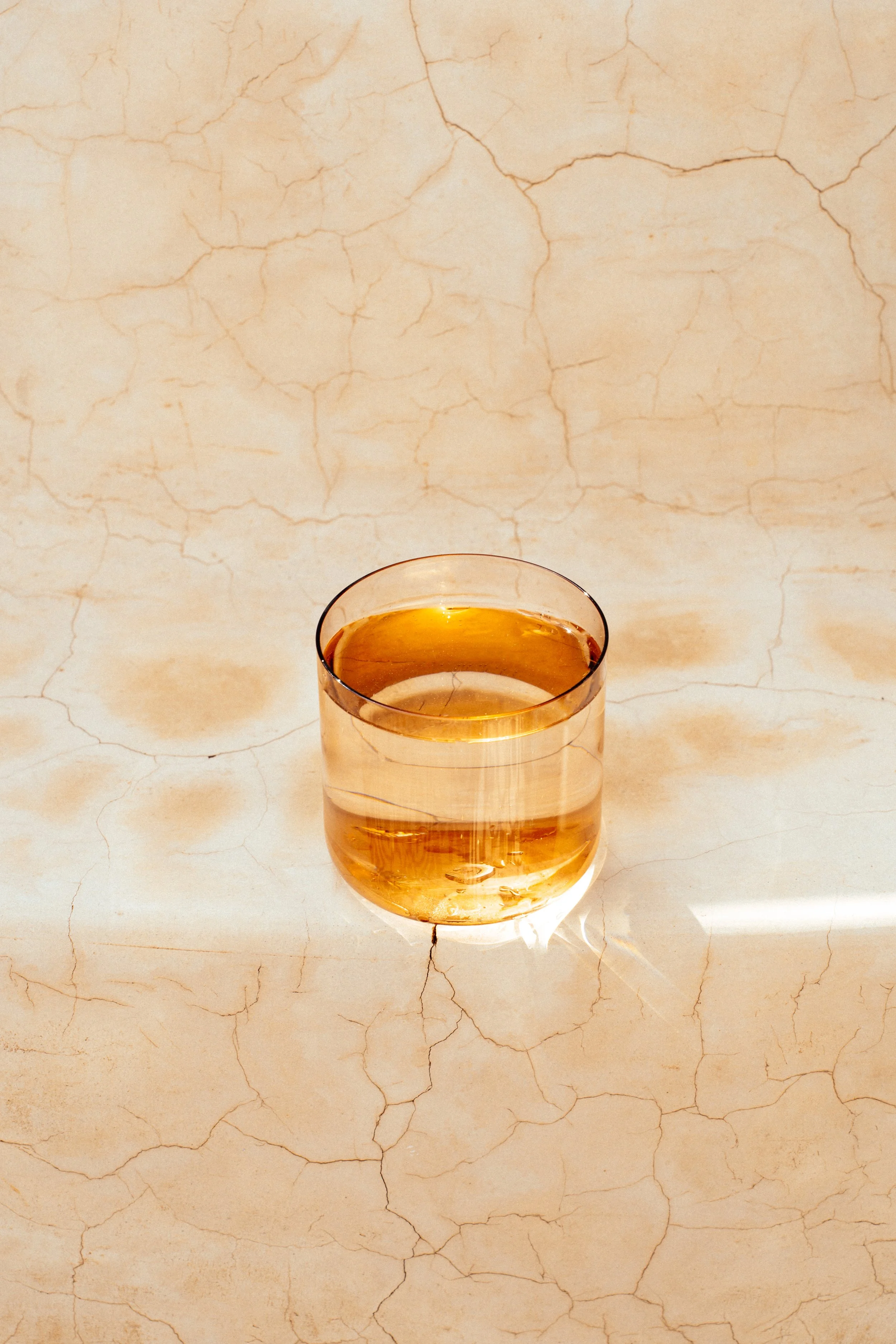 Ein Glas mit bernsteinfarbenem Getränk auf einer beigen, rissigen Oberfläche.