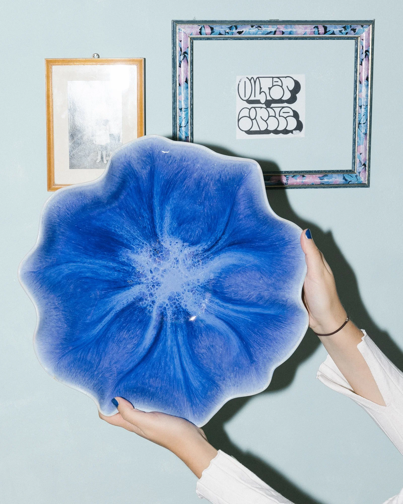 Person hält eine blaue, keramische Schale vor einer hellblauen Wand mit zwei Bilderrahmen.