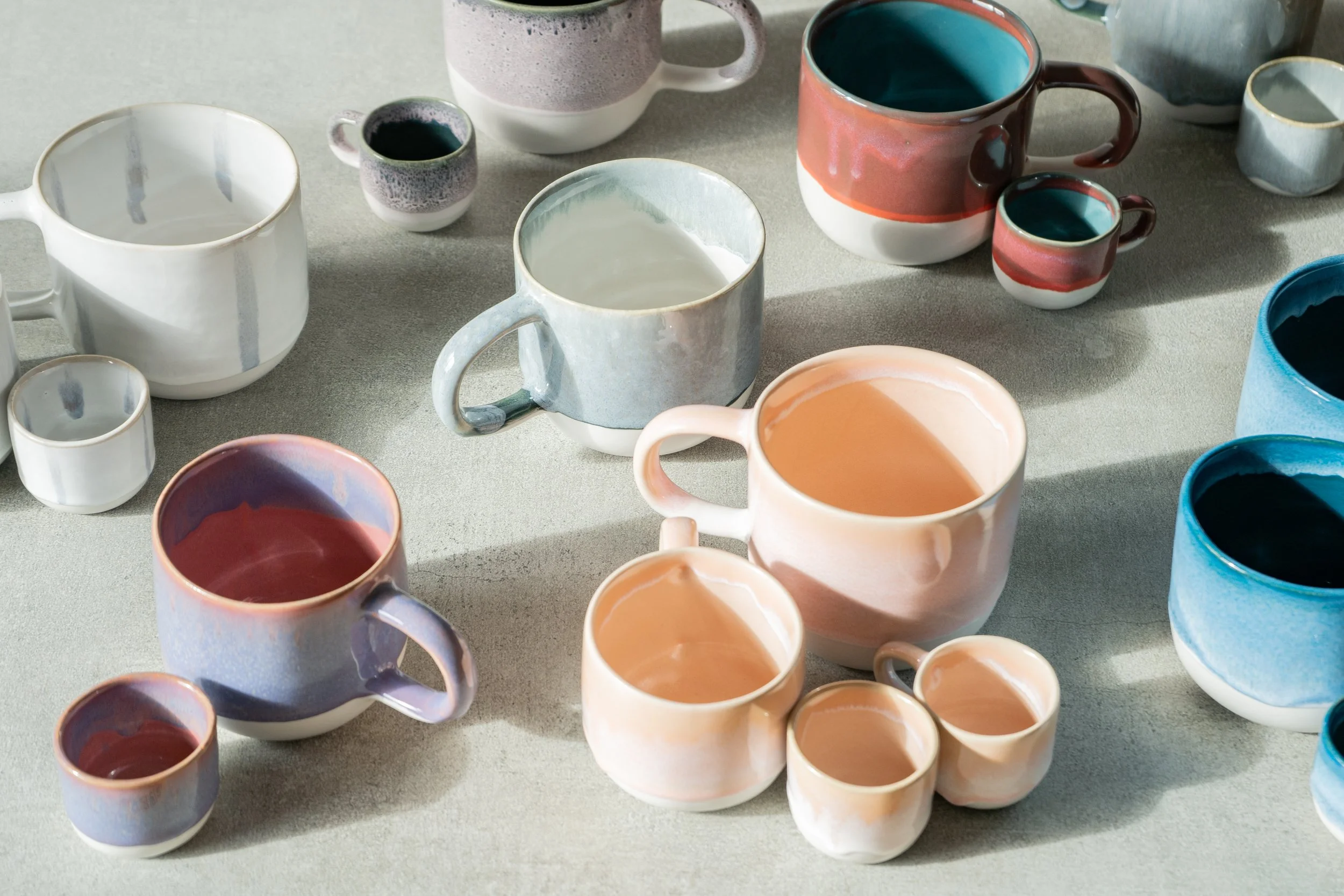 Verschiedene bunt bemalte Keramik-Tassen und -Becher auf einer hellen Oberfläche