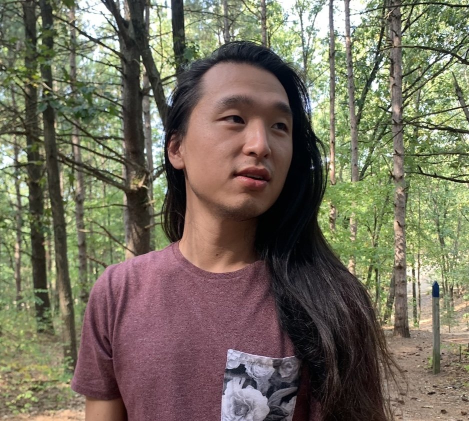 Sean Cho Aryes standing in front of green trees and looking to his left.