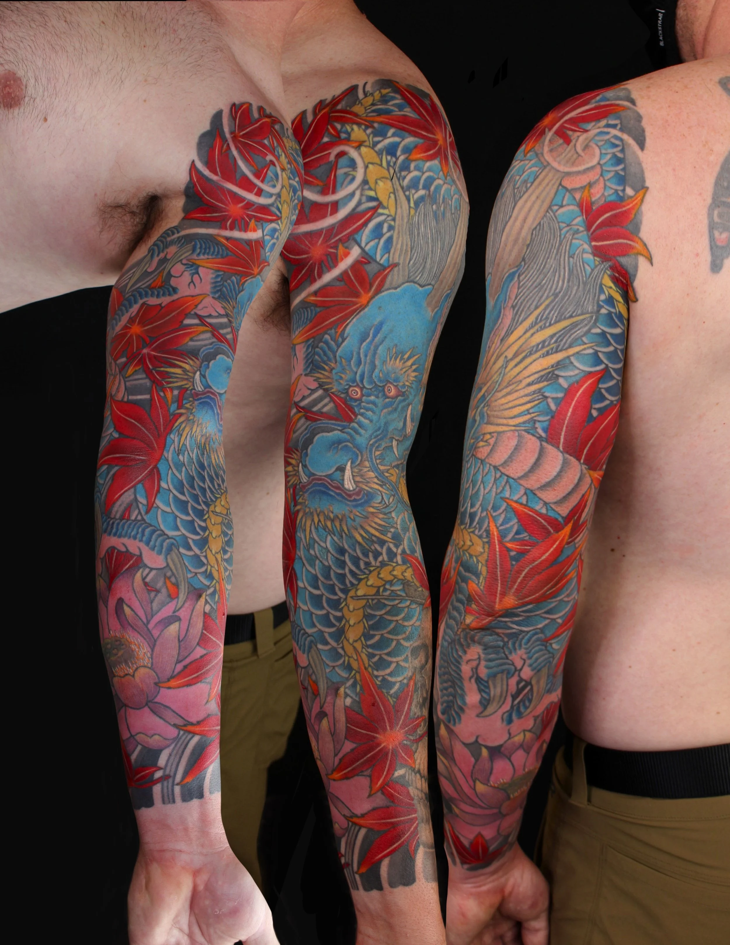 Two people with full arm tattoos featuring colorful Japanese-style dragons and floral designs, standing close together, partially shirtless.