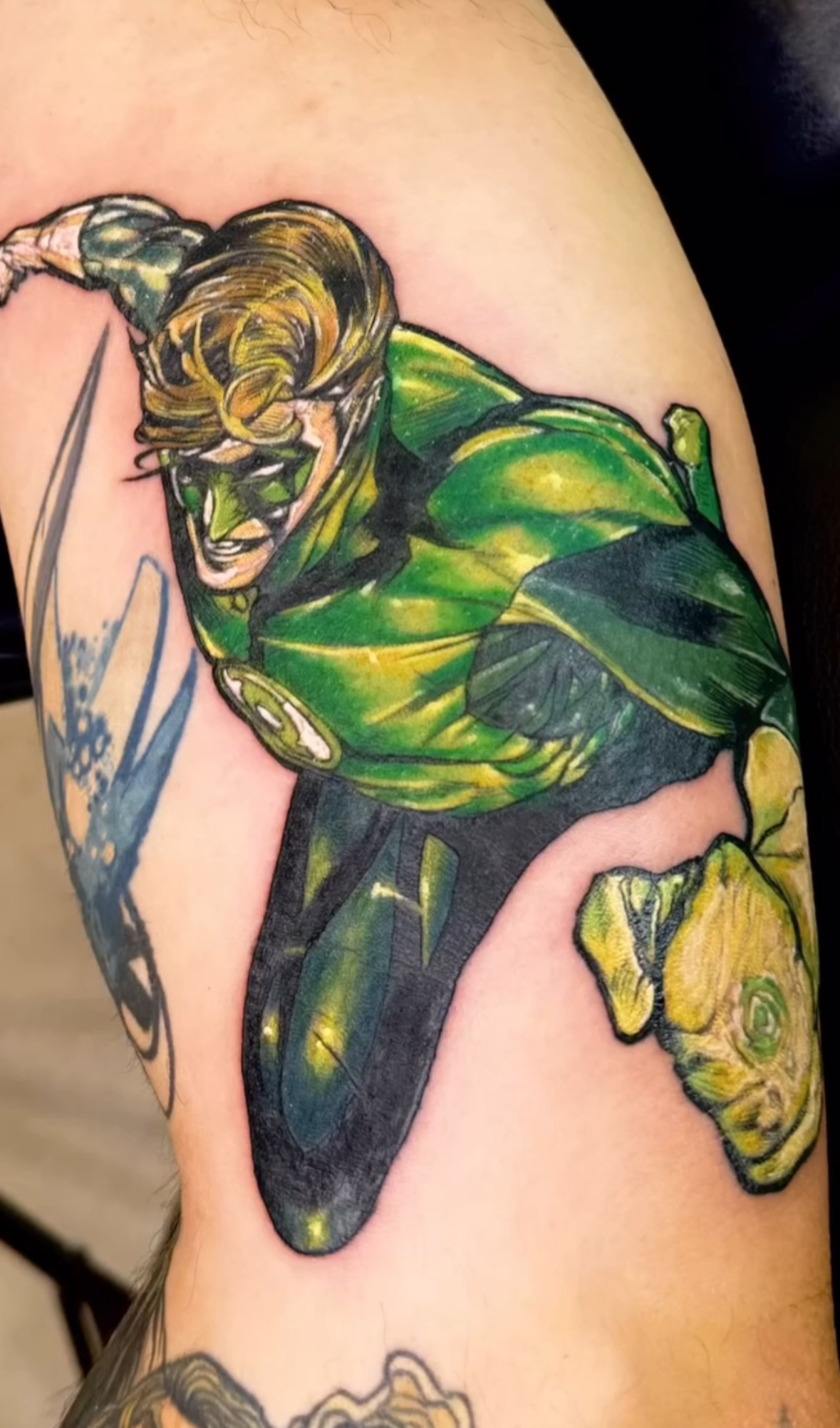 Colorful tattoo of a comic book style Green Lantern superhero in a dynamic pose on person's upper arm.