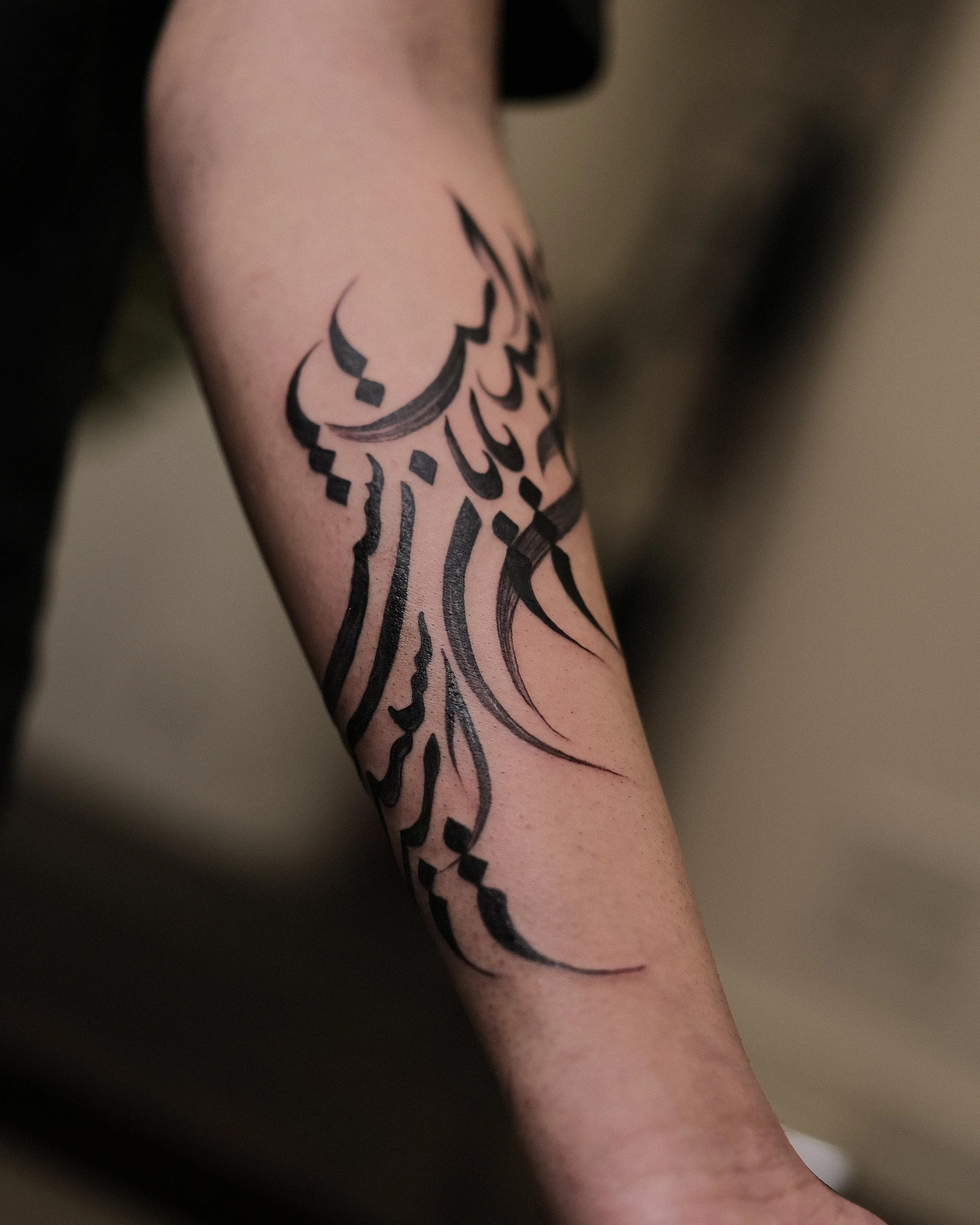 Black tribal-style tattoo on the forearm with abstract lines and shapes.