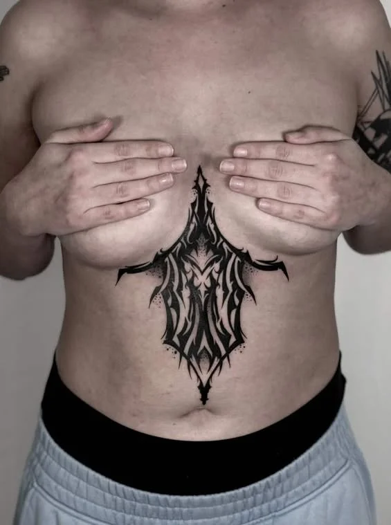 Person covering their chest with hands, displaying a large black tribal-style tattoo on the chest and abdomen.