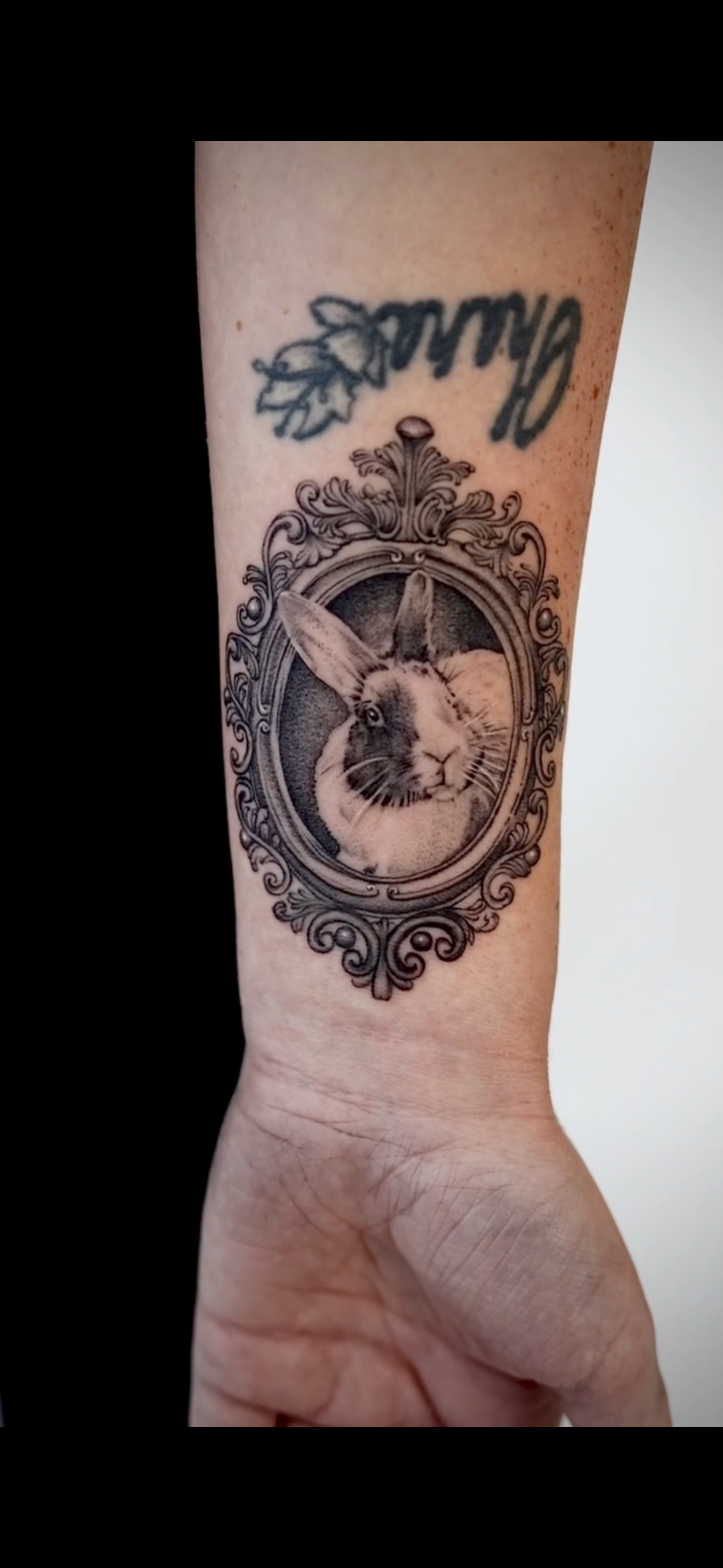Tattoo of a rabbit's head in an ornate oval frame on person's forearm.