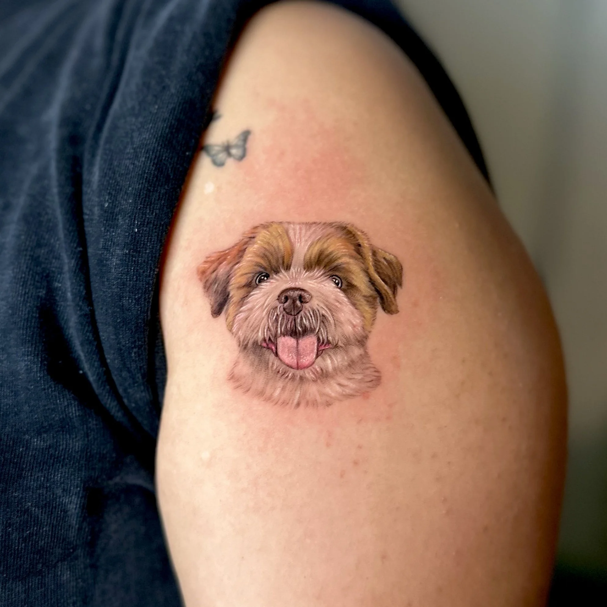 Colorful tattoo of a happy dog's face on a person's upper arm, with the dog sticking out its tongue.