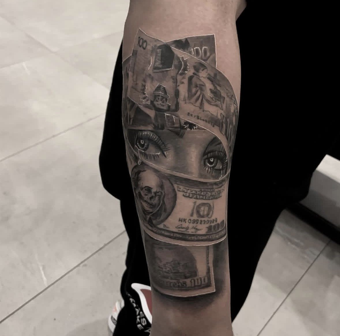 A tattoo on a person's arm that depicts various images including a pair of realistic eyes, a dollar bill, and a city skyline.