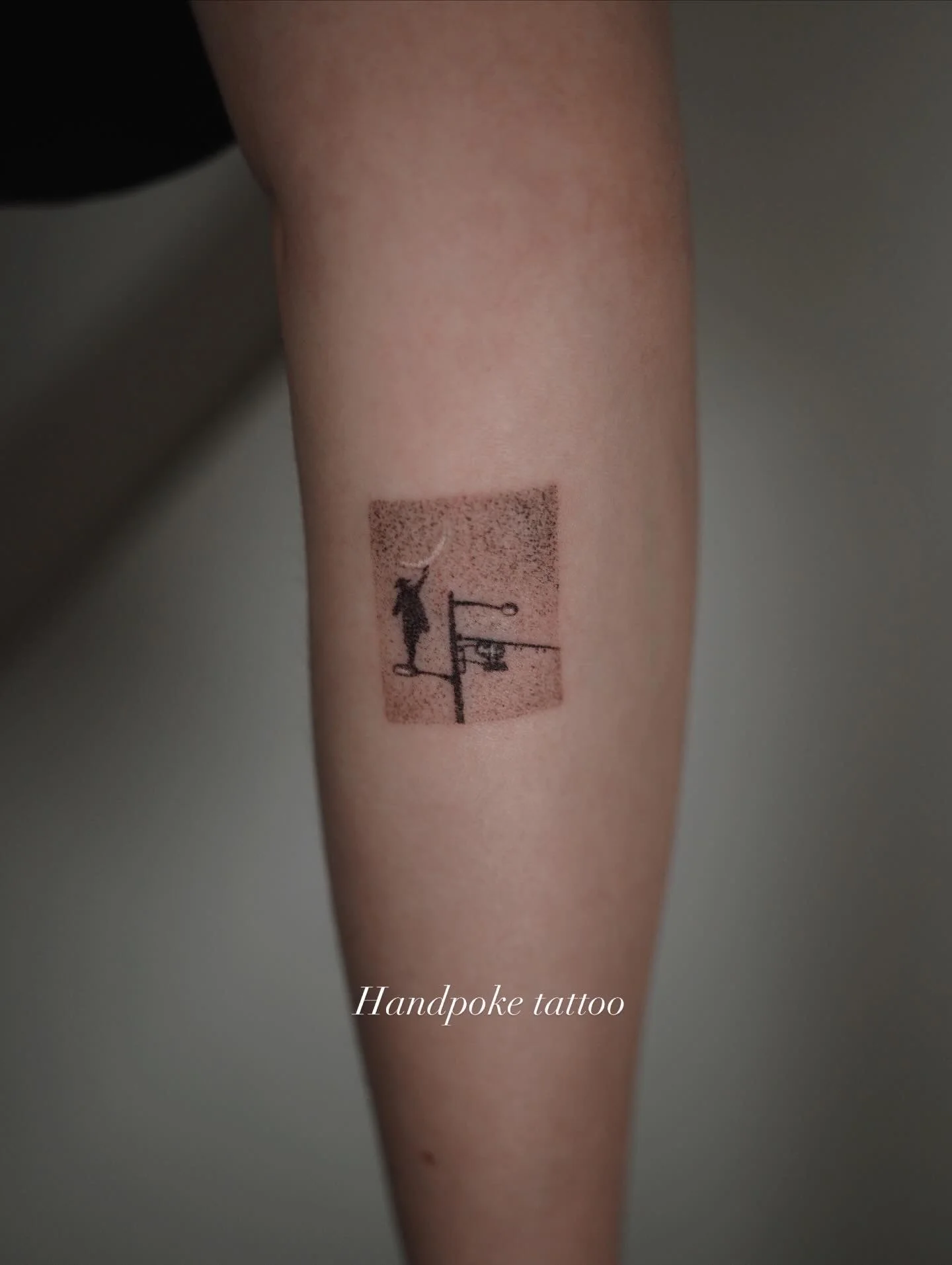 Tattoo of a figure reaching up on a pole with a hanging hook, on a person's forearm, with the words 'Handpoke tattoo' written below.