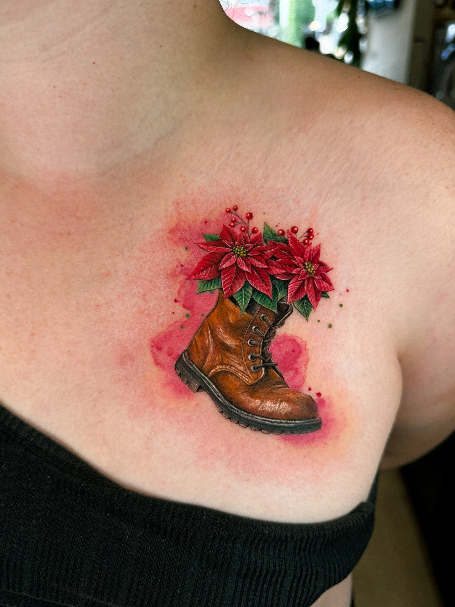 Tattoo of a brown leather boot with red poinsettia flowers and green leaves emerging from the top, on a person's chest.