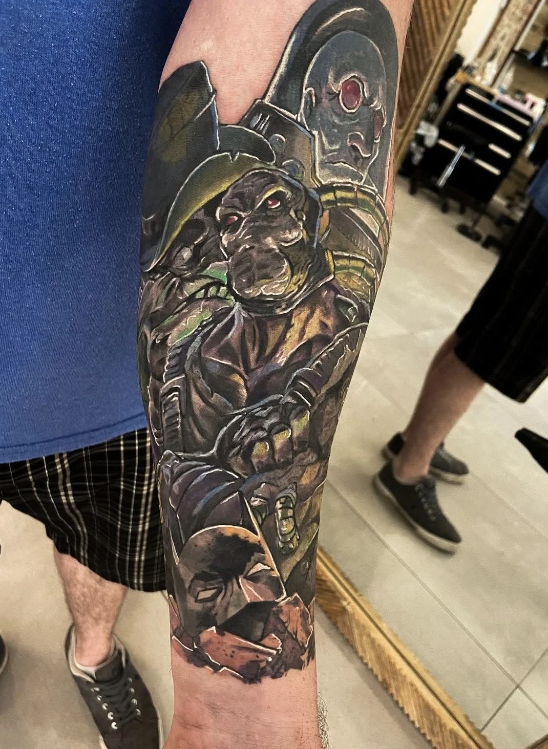 Colorful tattoo sleeve featuring characters from science fiction or video games, including a humanoid robot, a dog dressed like a soldier, and a human face at the bottom.