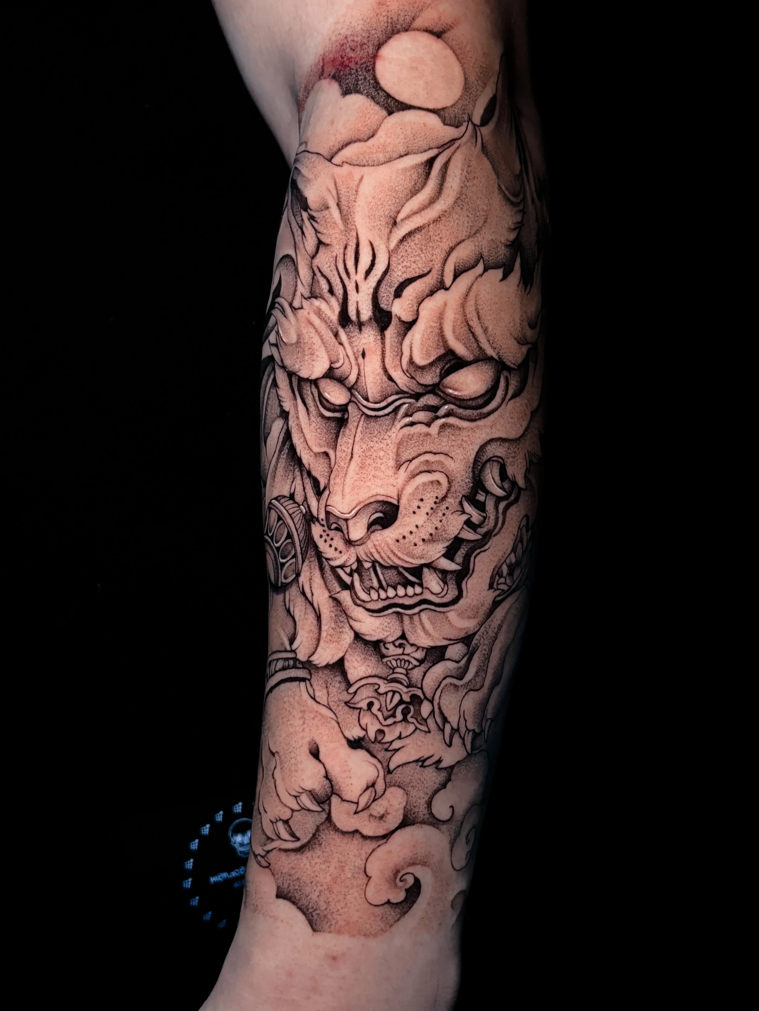 Tattoo of a traditional Japanese lion or tiger face with clouds and swirling motifs on a person's arm.