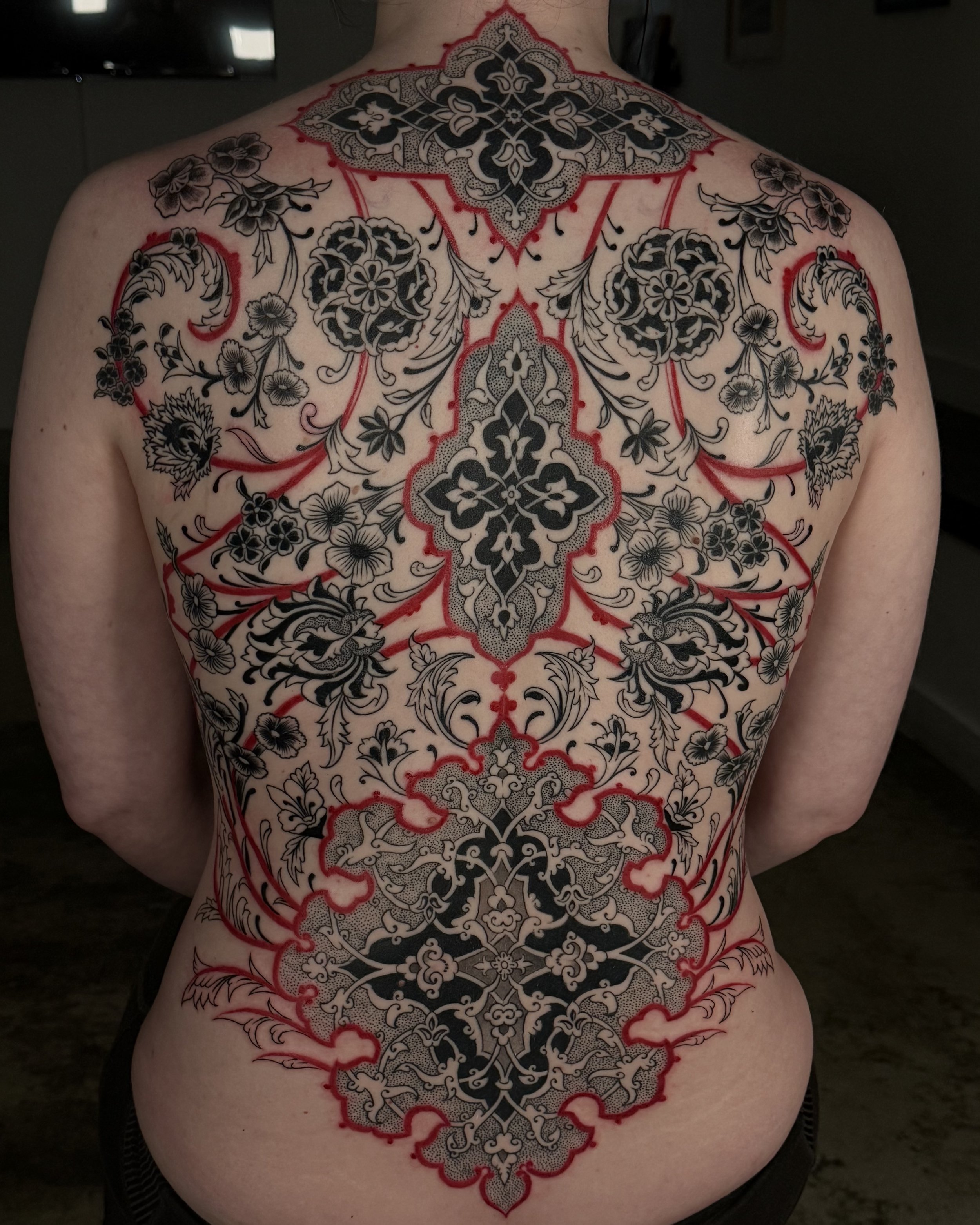 A person's back featuring an intricate, large black and gray floral tattoo with red outlines.