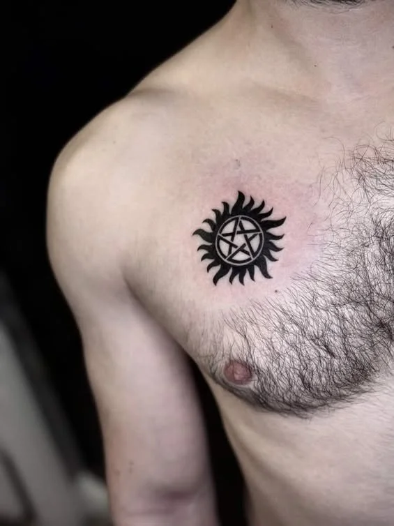 Tattoo of a sun with a pentagram inside on a person's upper chest near the shoulder.