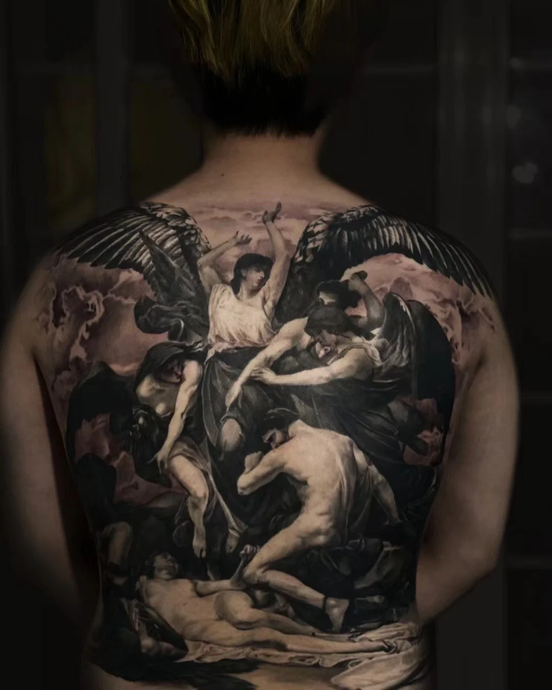 Detailed black and gray tattoo covering person's back depicting a classical scene with angels and human figures in dynamic poses.