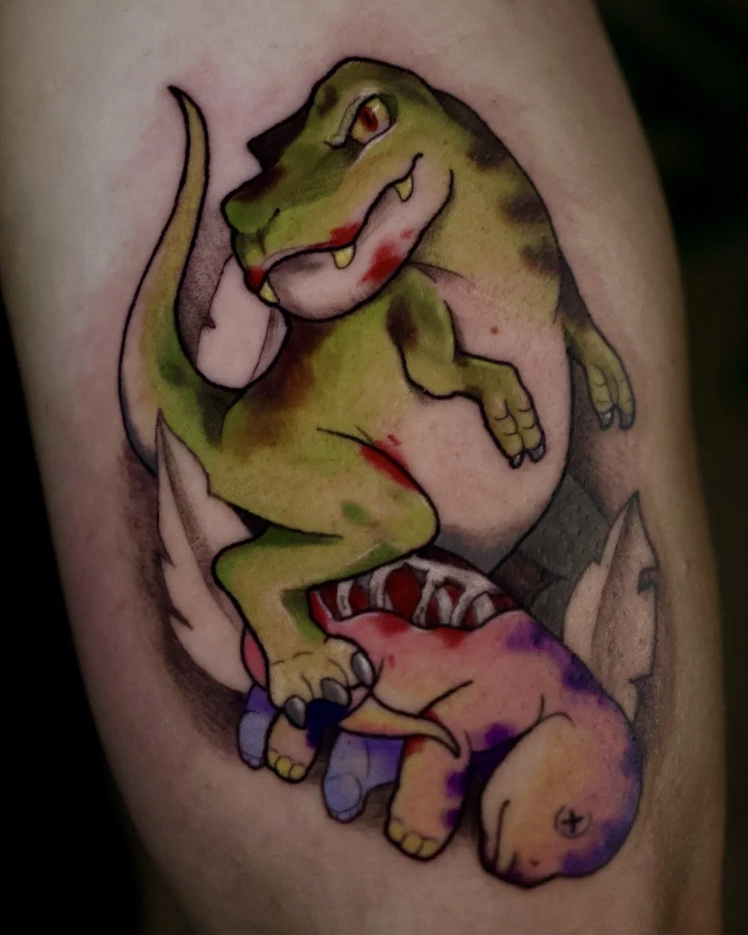 A colorful tattoo of a cartoon dinosaur on skin, with a green body, red eyes, and a playful expression, surrounded by abstract designs.