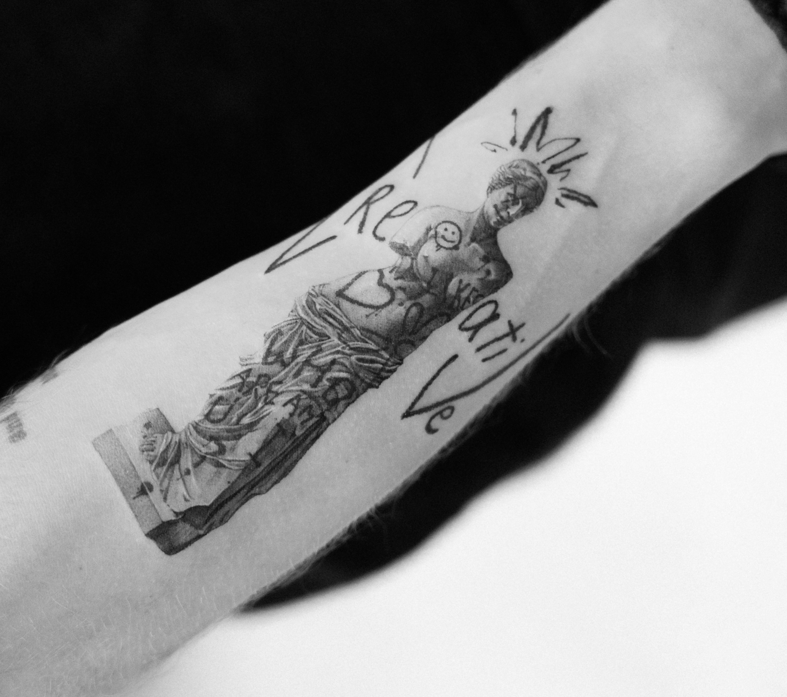 Tattoo of a religious figure holding a small heart, with text that reads 'In Jesus I Trust' on a person's arm.