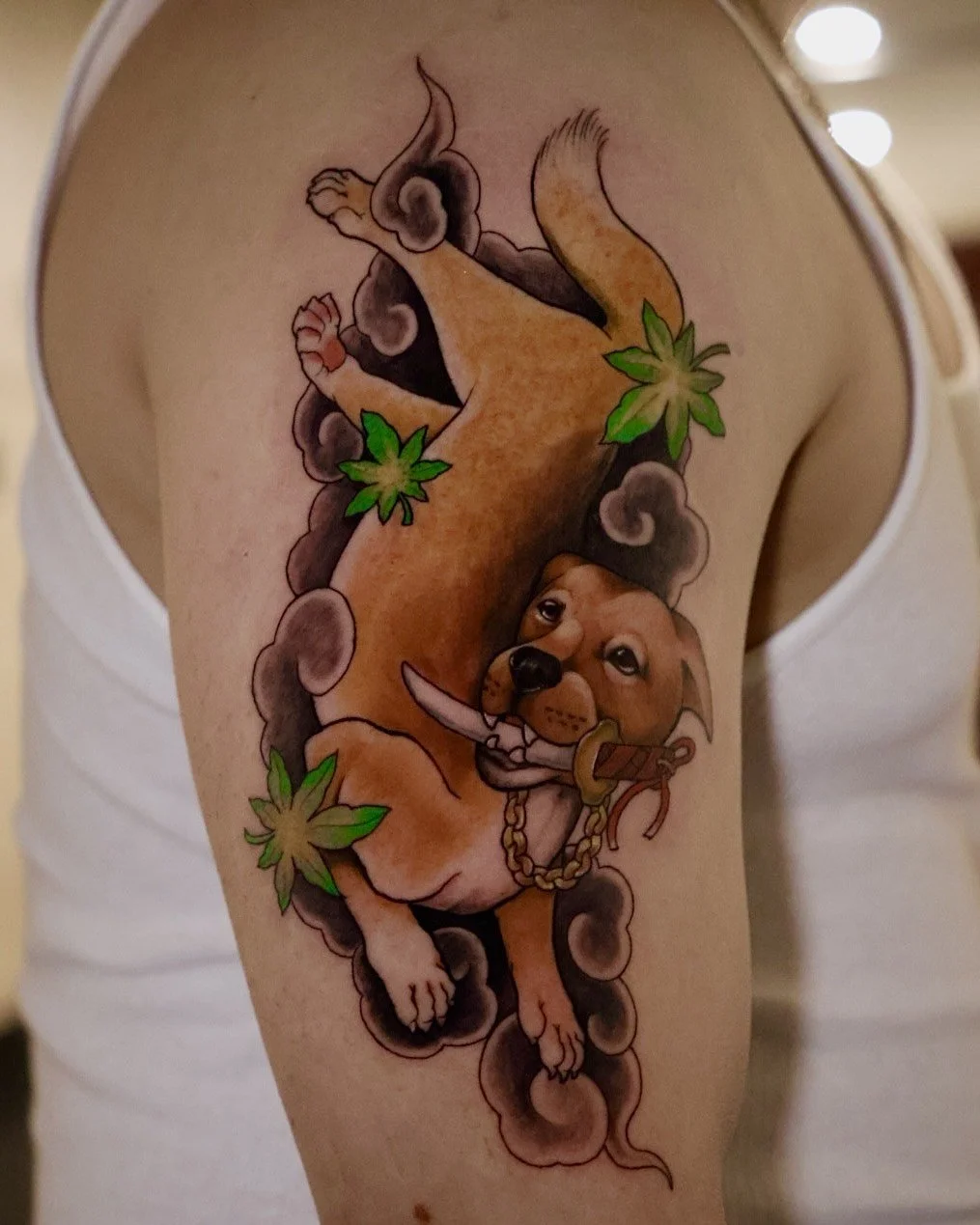 Tattoo of a playful dog with a bone, surrounded by smoke and cannabis leaves.