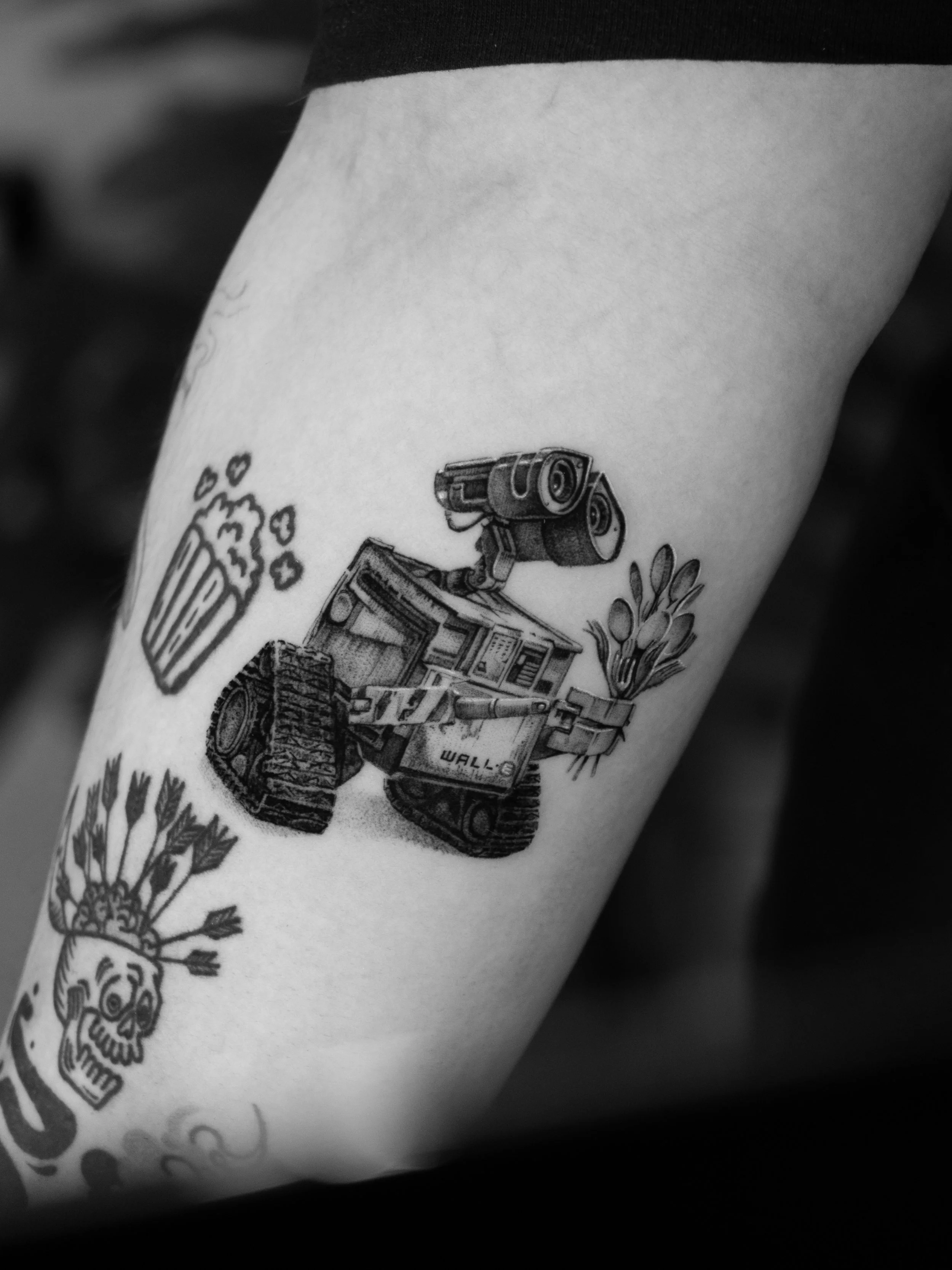 Black and white tattoo of WALL-E, a robot from the animated film, holding a bunch of leaves.