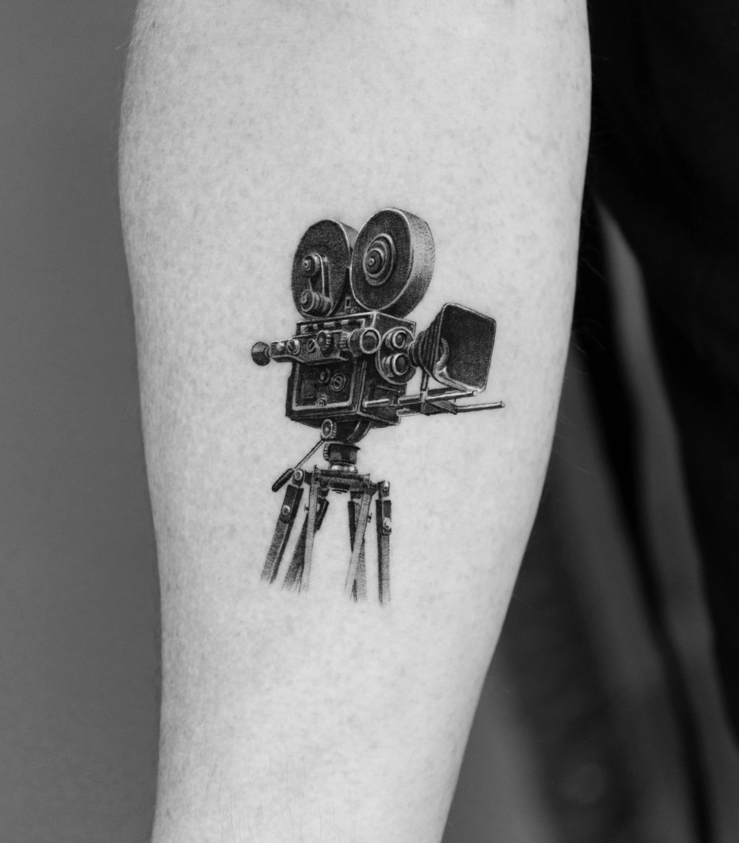 Black and white tattoo of an old-fashioned film camera on a person's arm.