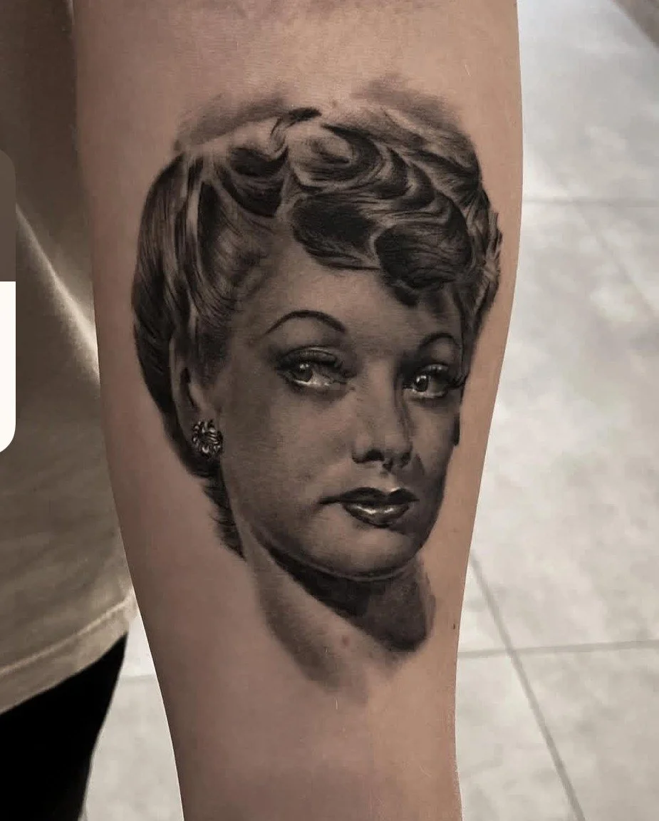 Black and gray tattoo of a woman's face on a person's upper arm.