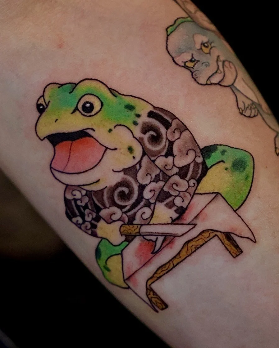 Colorful tattoo of a smiling cartoon dinosaur with a yellow and green head sitting at a table.