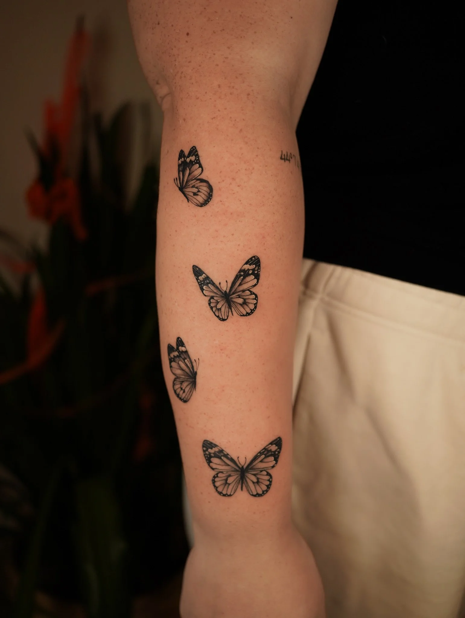 Four black and white butterfly tattoos on a person's forearm.