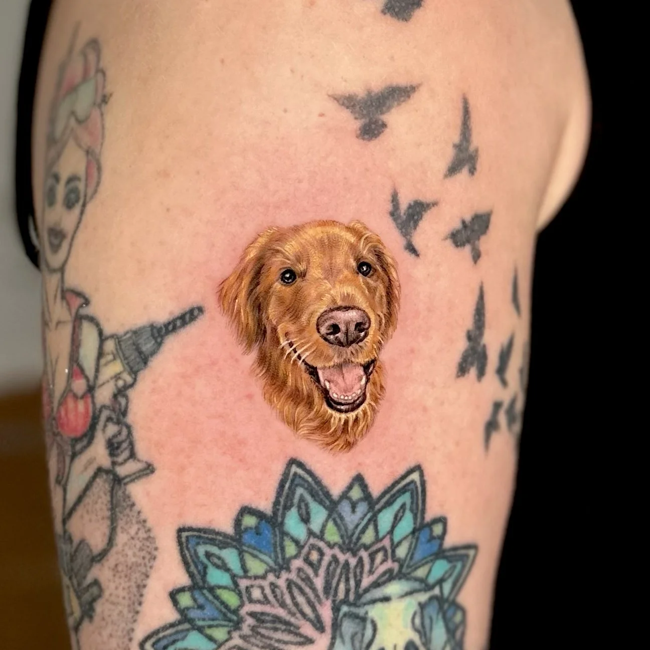 Tattoo of a realistic dog’s head with a happy expression, brown fur, and open mouth, on a person's upper arm.