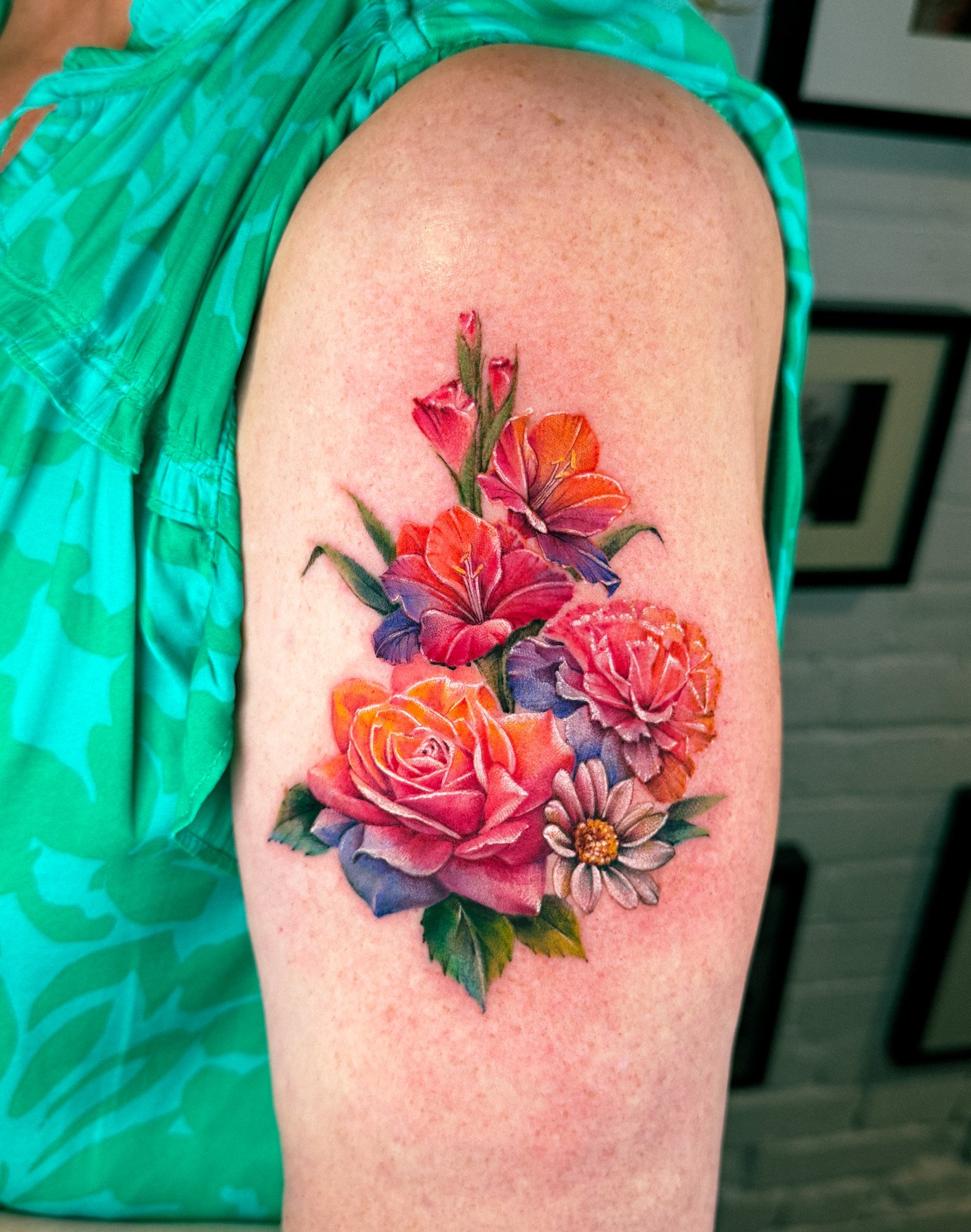 A colorful tattoo of various flowers, including roses, lilies, and daisies, on a person's upper arm.