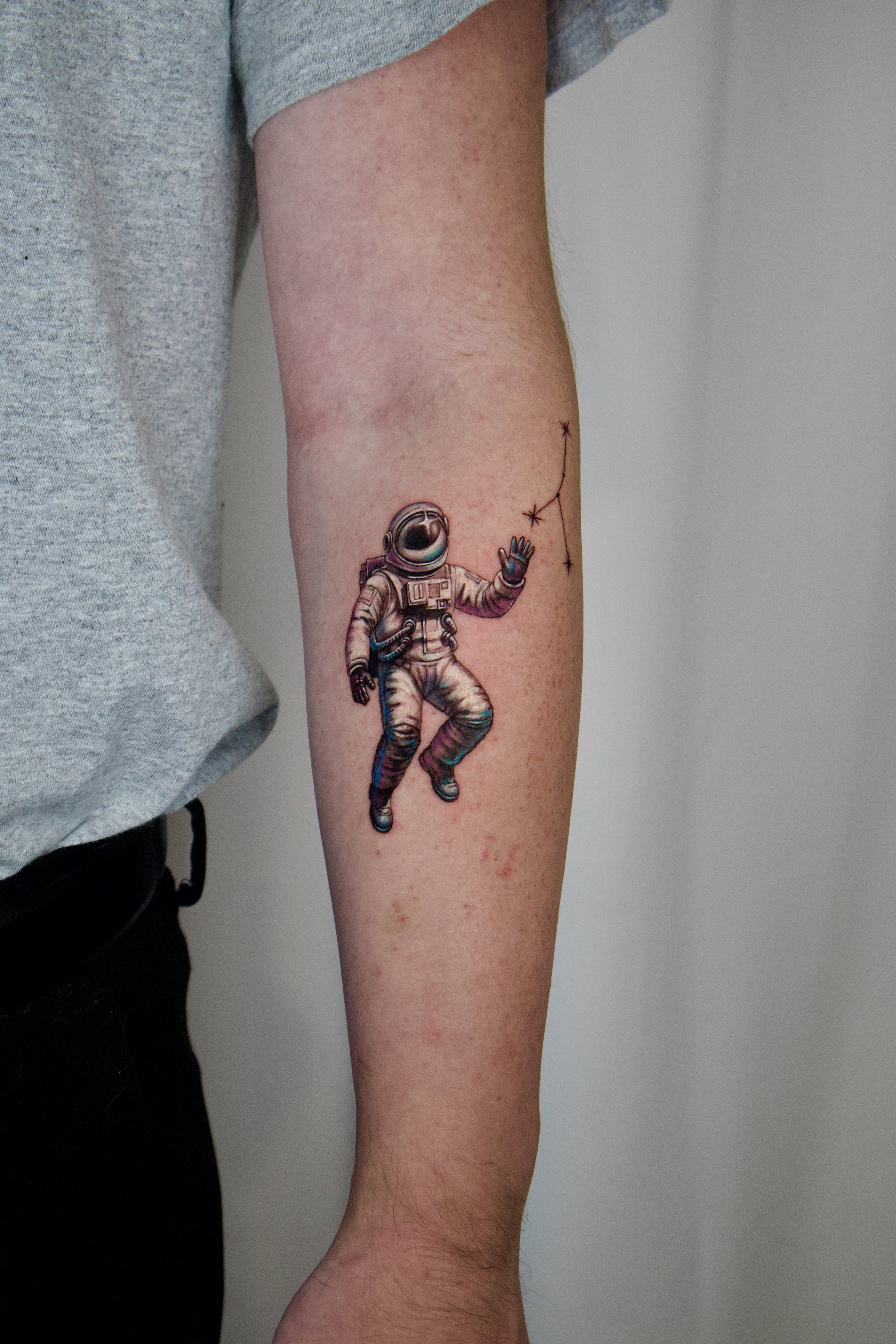 Tattoo of an astronaut floating in space, reaching with one hand towards a small constellation on the forearm.
