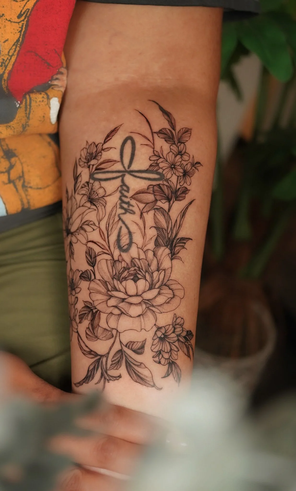 Black and gray floral tattoo on person's arm with a word written vertically.